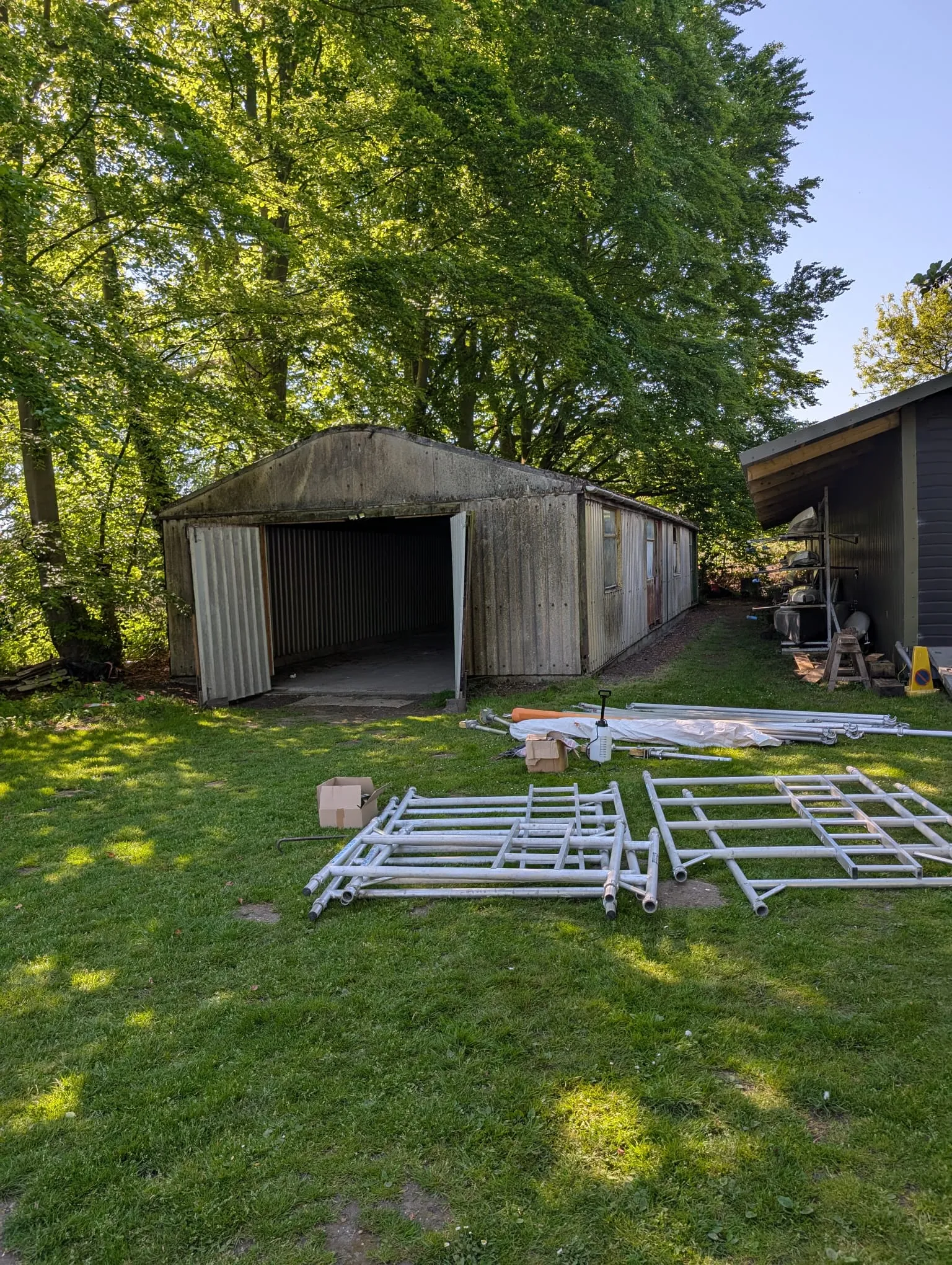 An old garage with an asbestos roof and panels, surrounded by grass and trees, with equipment ready for removal work.