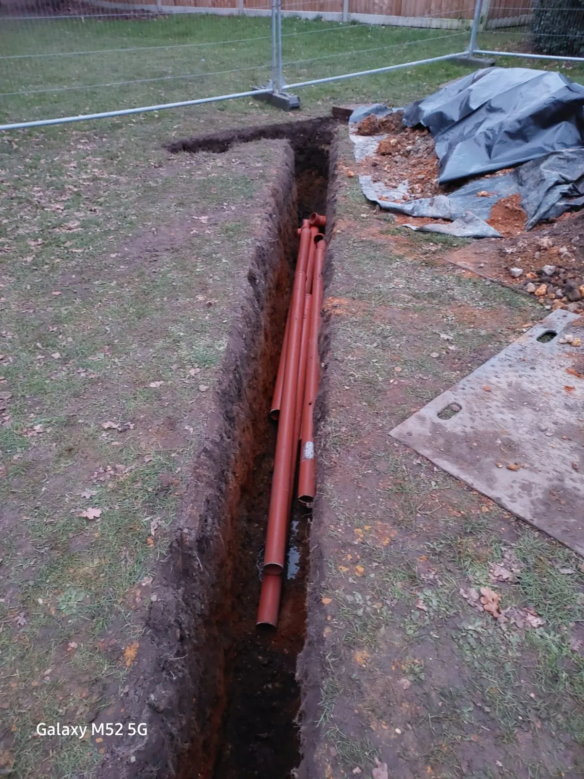 A trench dug in a garden with orange drainage pipes being installed for a new connection or repair.