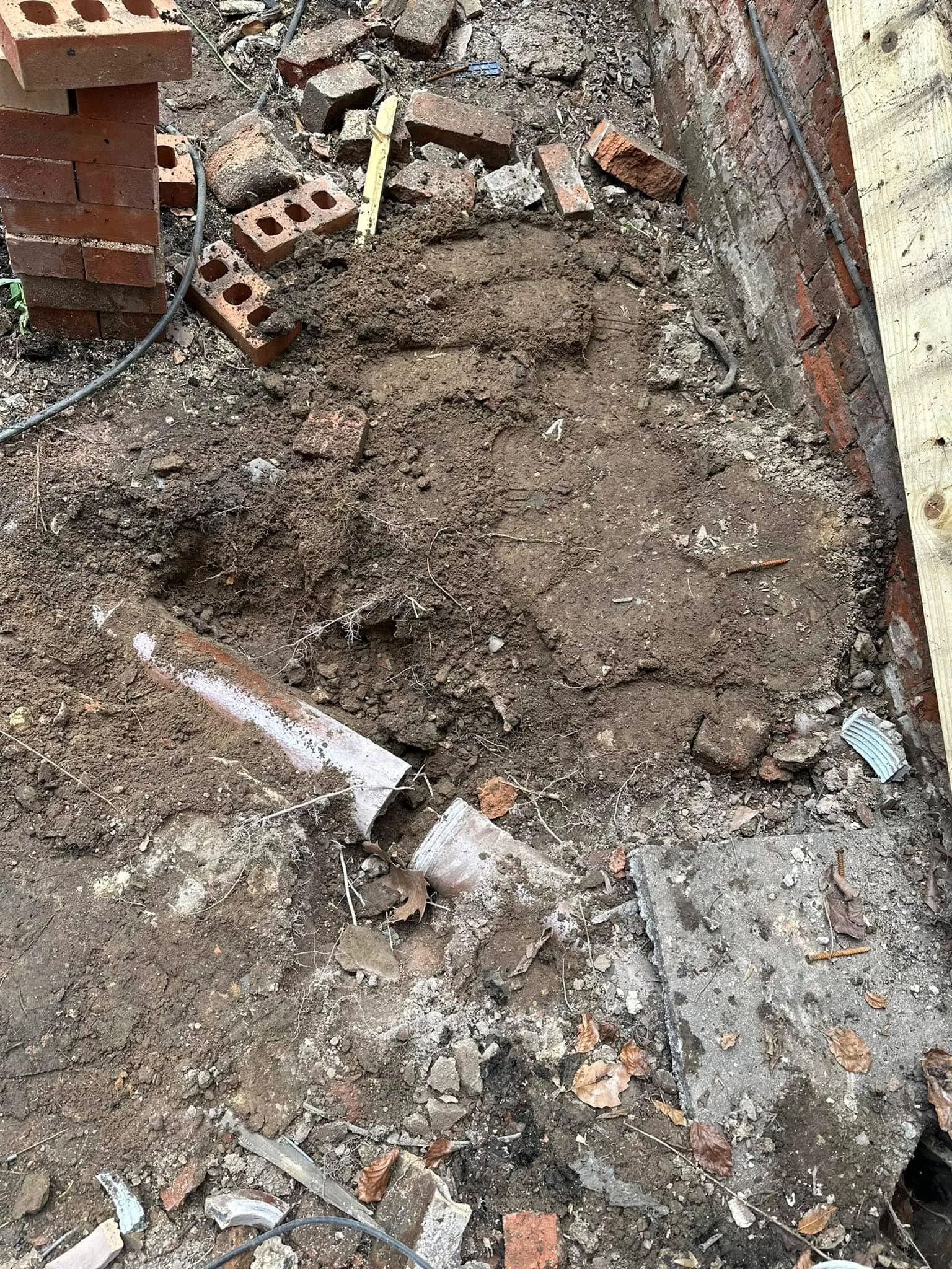 Excavated ground with exposed, damaged drainage pipe during a repair or installation.
