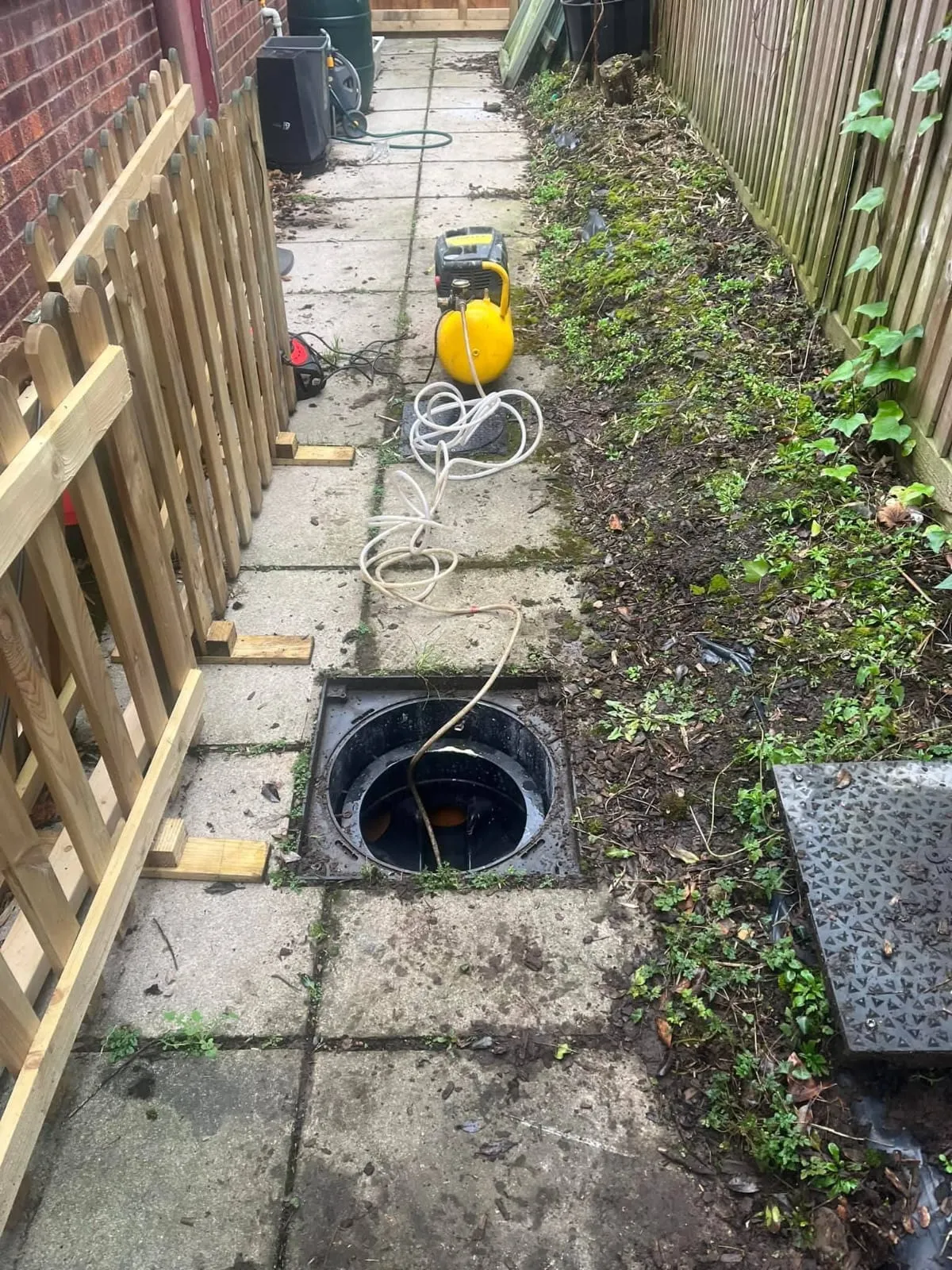 Open drain manhole with drainage equipment nearby.