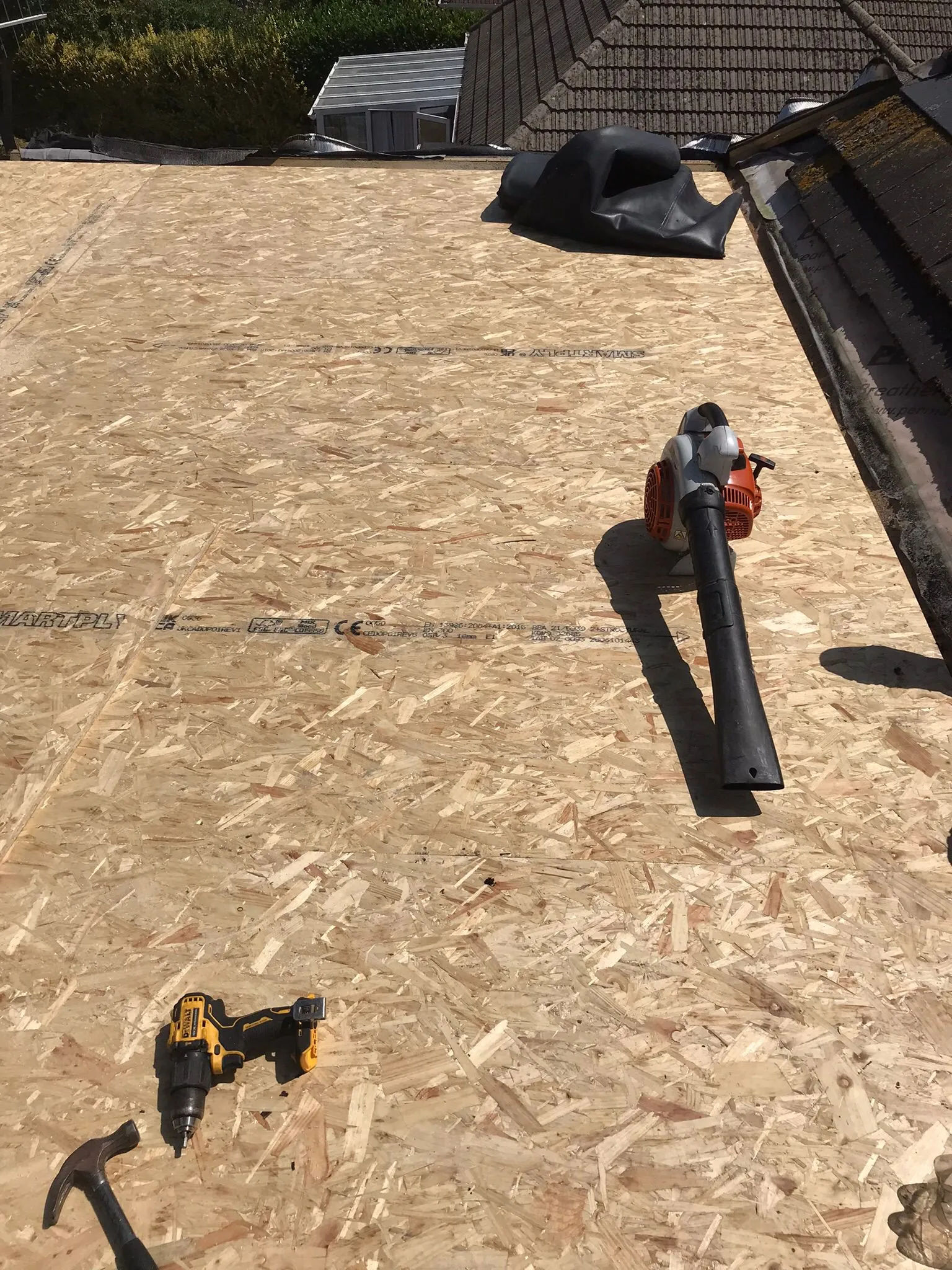 Roof under construction with OSB decking and roofing tools like a leaf blower, drill, and hammer.