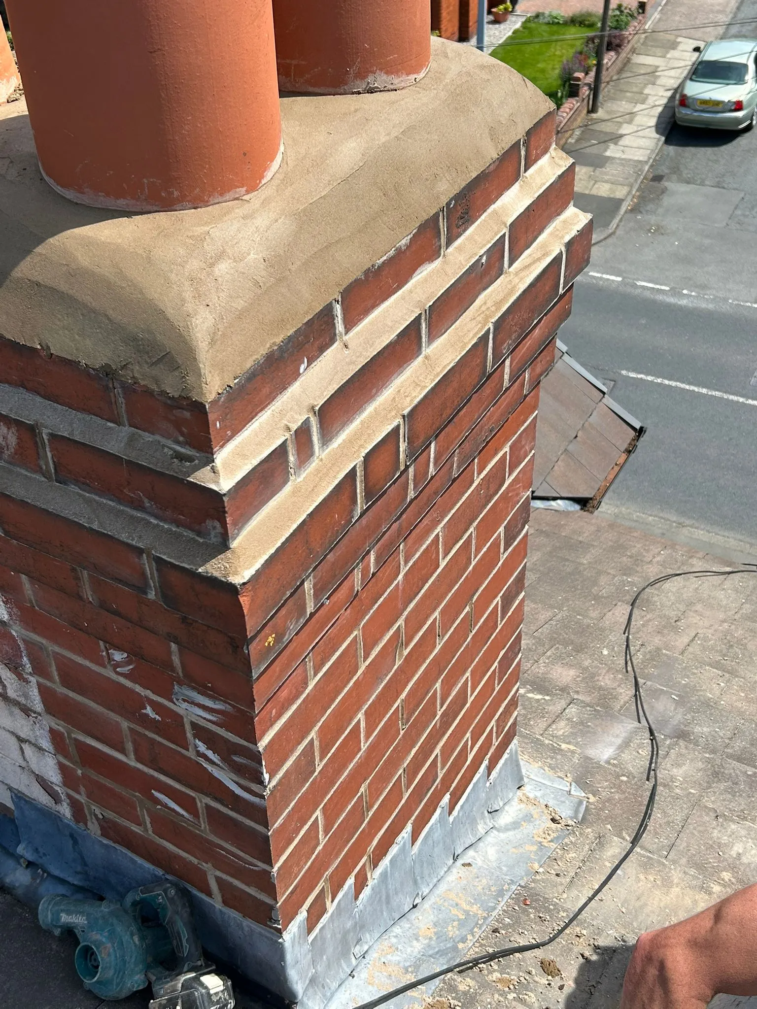 Close-up of a red brick chimney stack on a roof, with fresh mortar repointing and new lead flashing around its base.