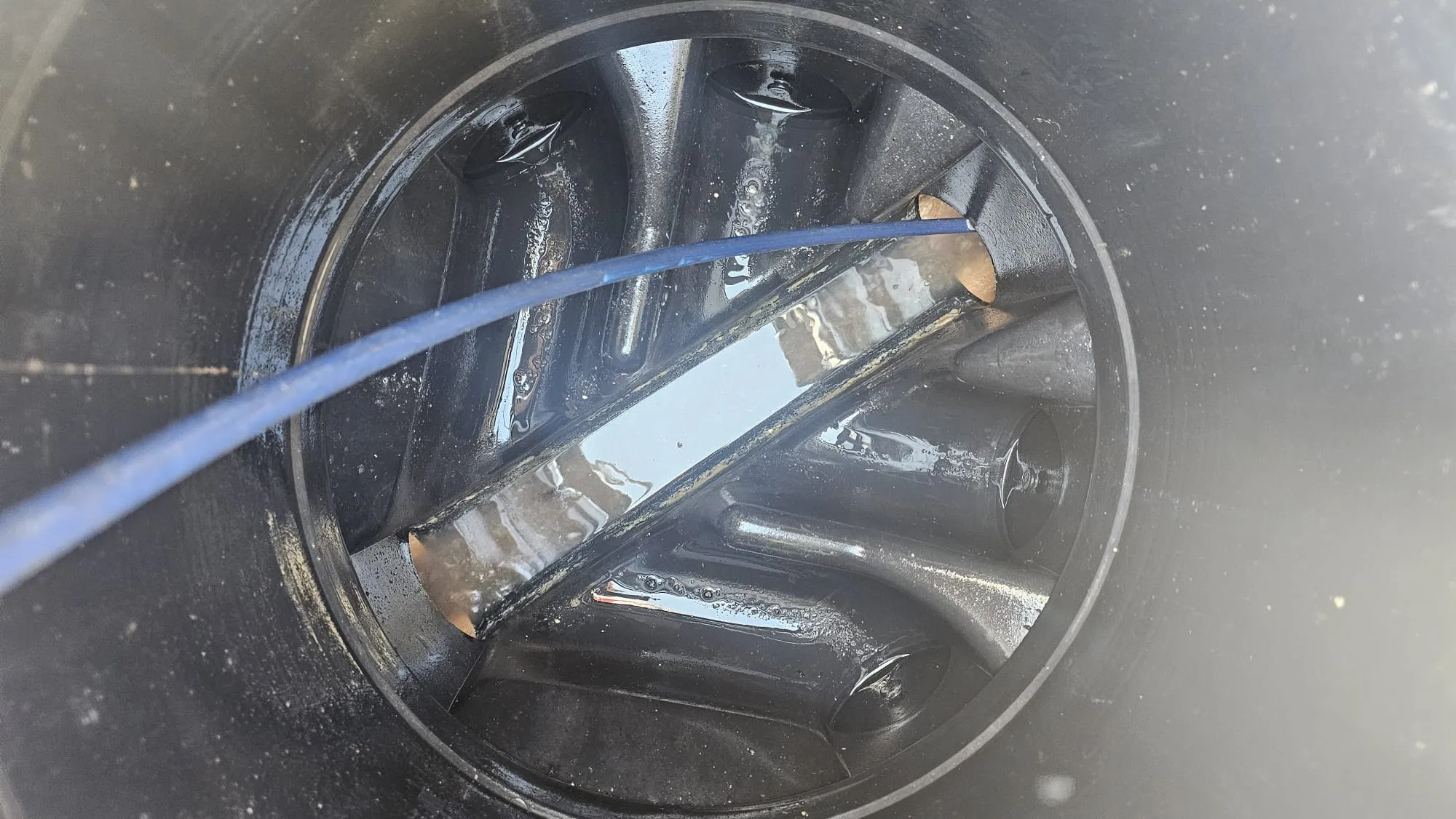 Inside a drain inspection chamber with standing water and a blue drainage tool inserted to clear a blockage.