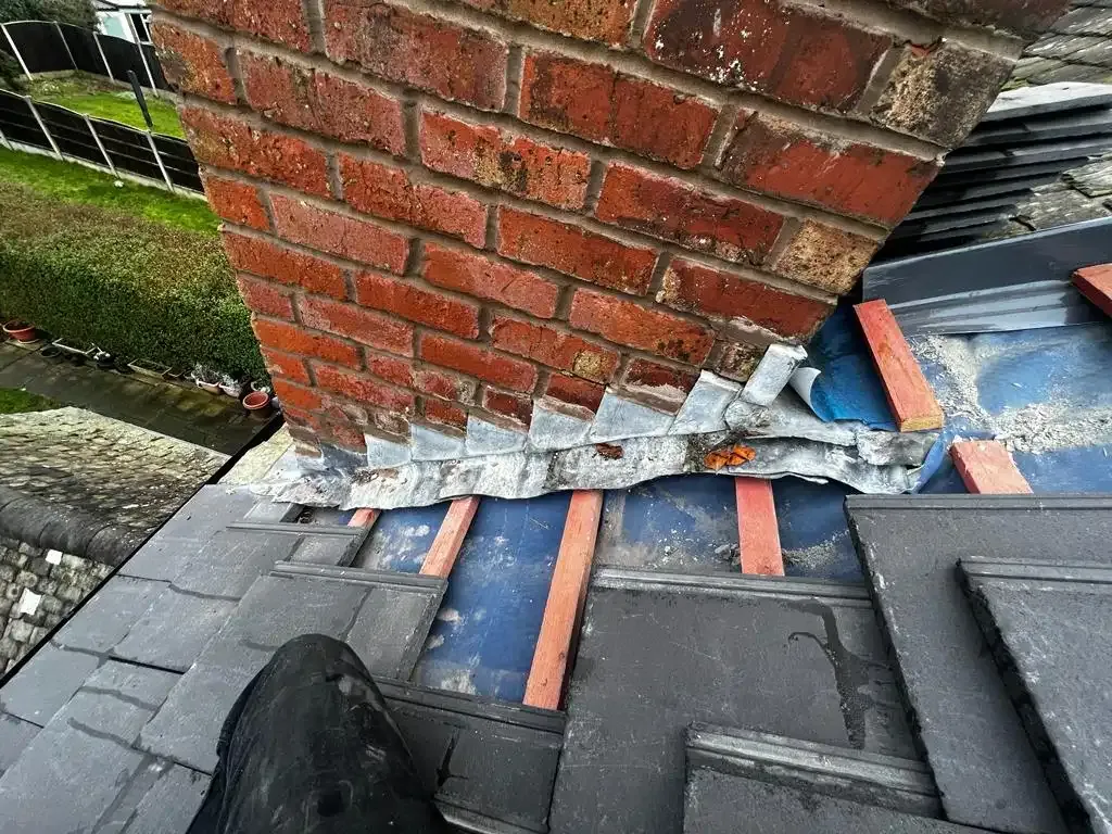 Roofers repairing a tiled roof around a chimney stack, with lead flashing visible.