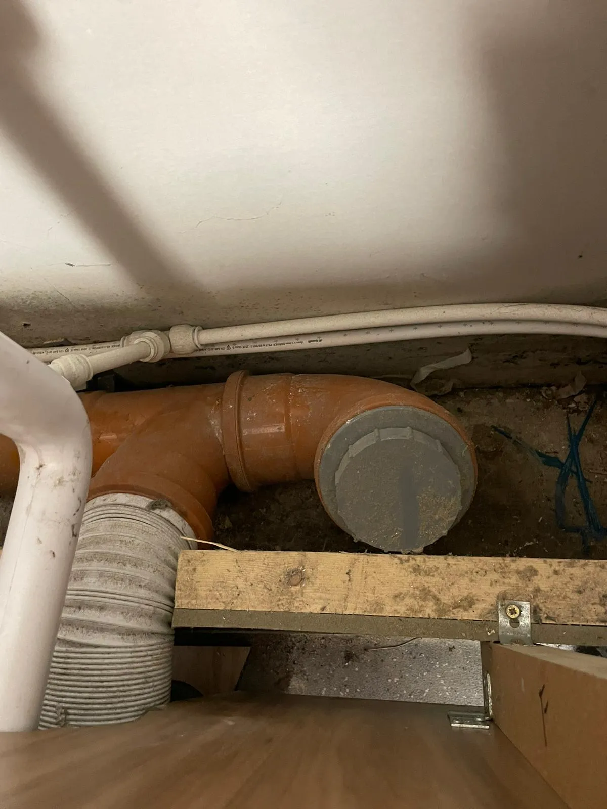 Orange drainage pipes with a grey cap, and other utility lines, visible under a floor or in a crawl space.