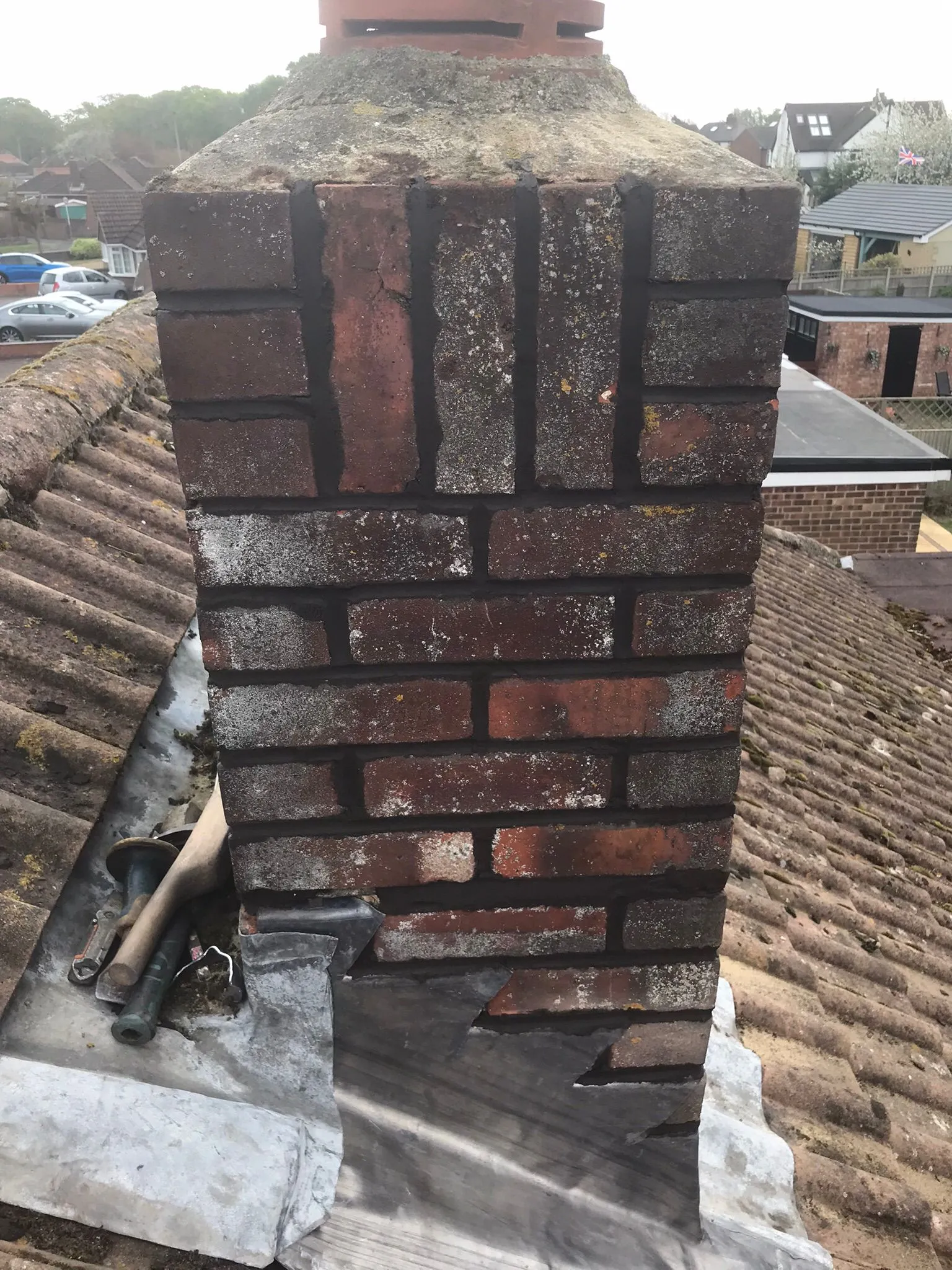A brick chimney on a tiled roof with lead flashing and roofing tools, illustrating a chimney repair project.