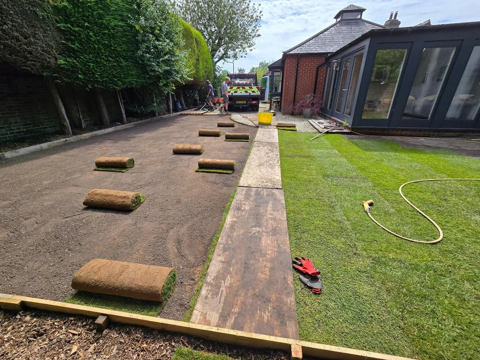 Newly laid natural turf in a garden with rolls of turf awaiting installation on prepared ground, highlighting garden landscaping work.