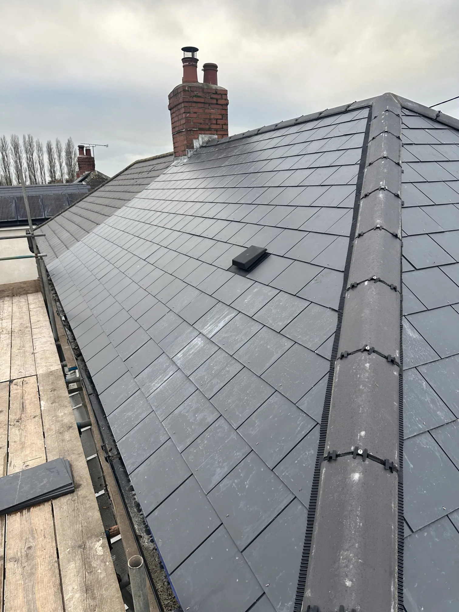 Newly installed dark grey tiled roof with dry ridge system and a chimney in the background.
