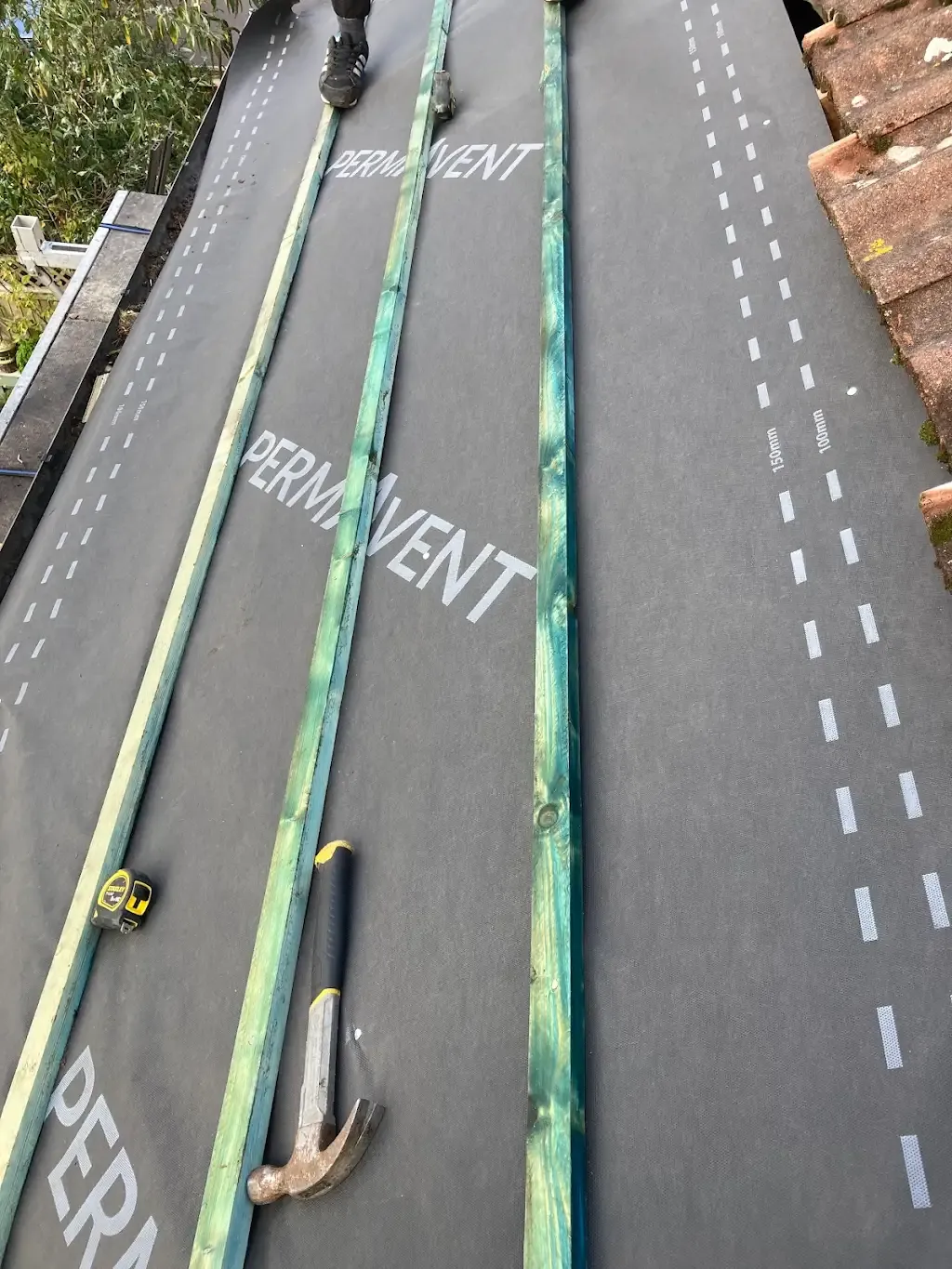 Installing roof underlayment and timber battens on a pitched roof.