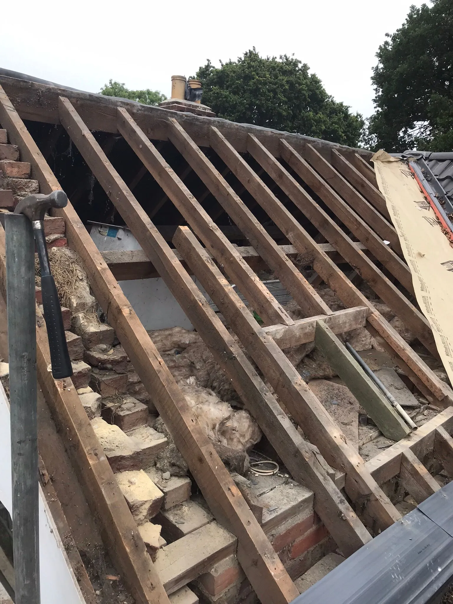 Exposed timber rafters and brickwork of a pitched roof during a new installation or significant repair on a house.