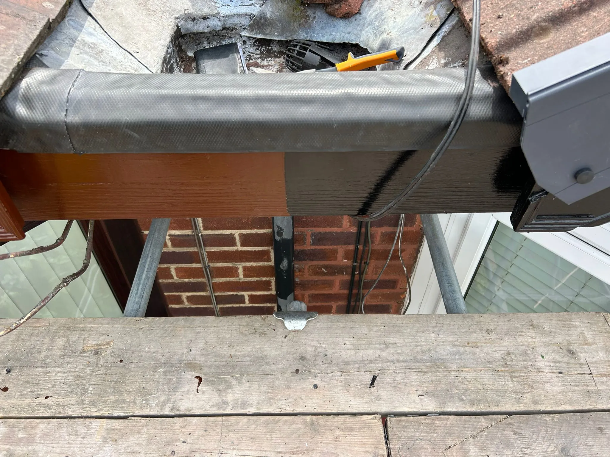 Installation of a flat roof edge, featuring a black waterproof membrane, a wooden fascia, and a grey gutter.