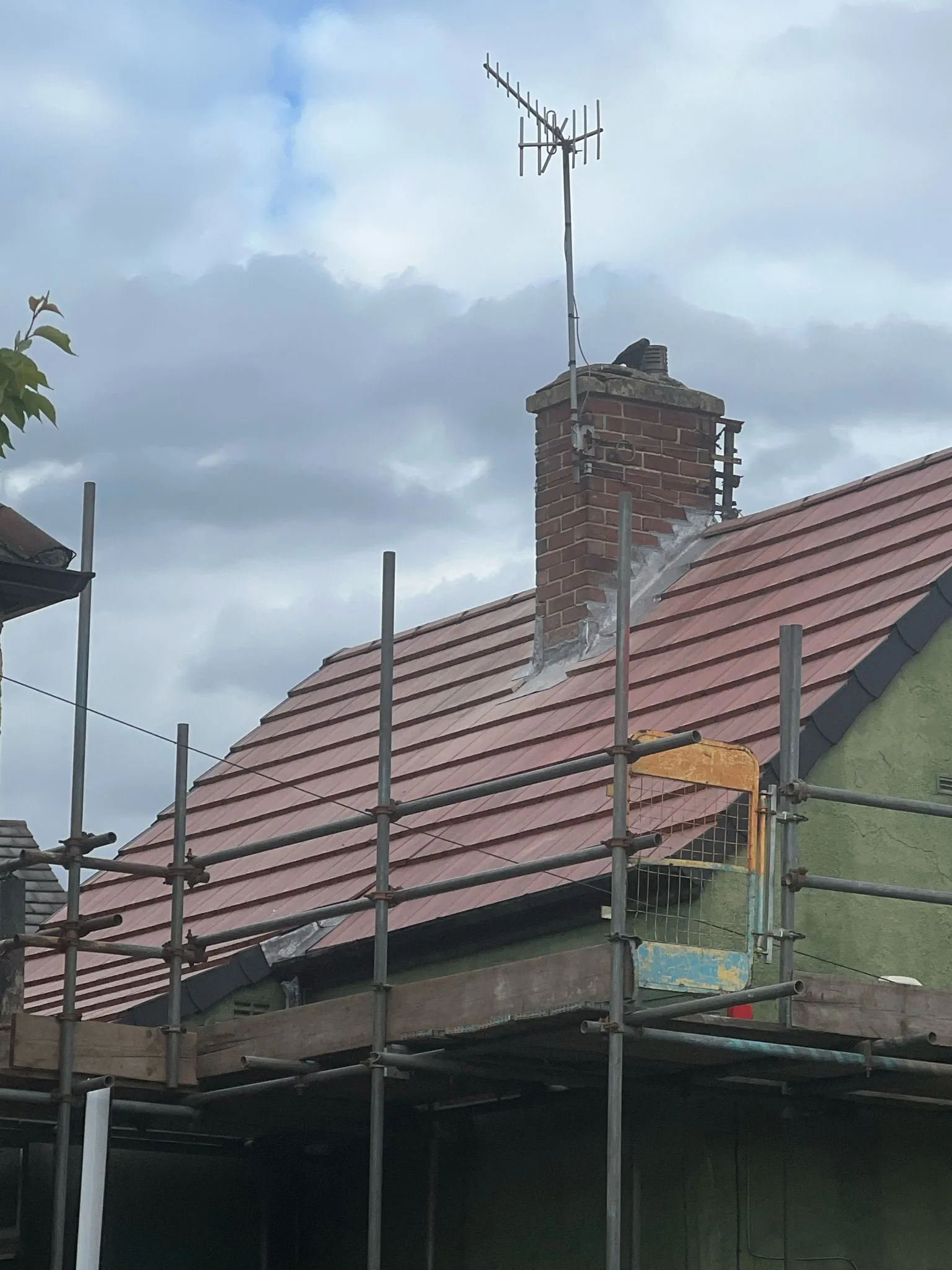 Pitched roof undergoing repair with scaffolding, chimney, and lead flashing