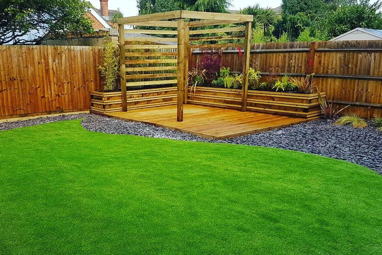 Recently completed garden landscaping with artificial grass, deck, pergola, and raised planters by Elite Construction Landscaping in Haywards Heath.