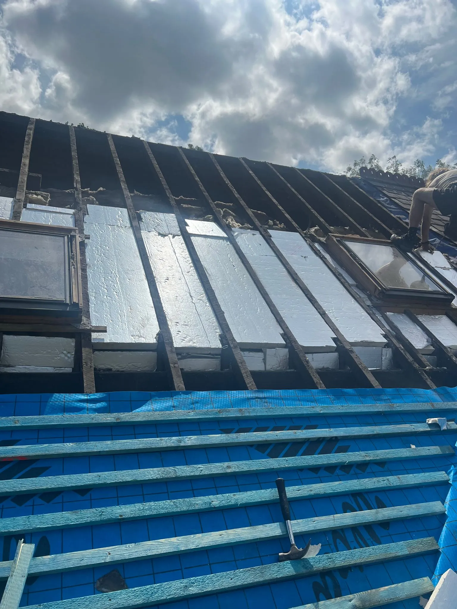 Pitched roof installation showing rafters, insulation, membrane, and battens with roof windows