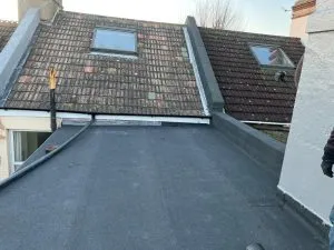Newly installed flat roof with a pitched tiled roof and Velux windows in the background