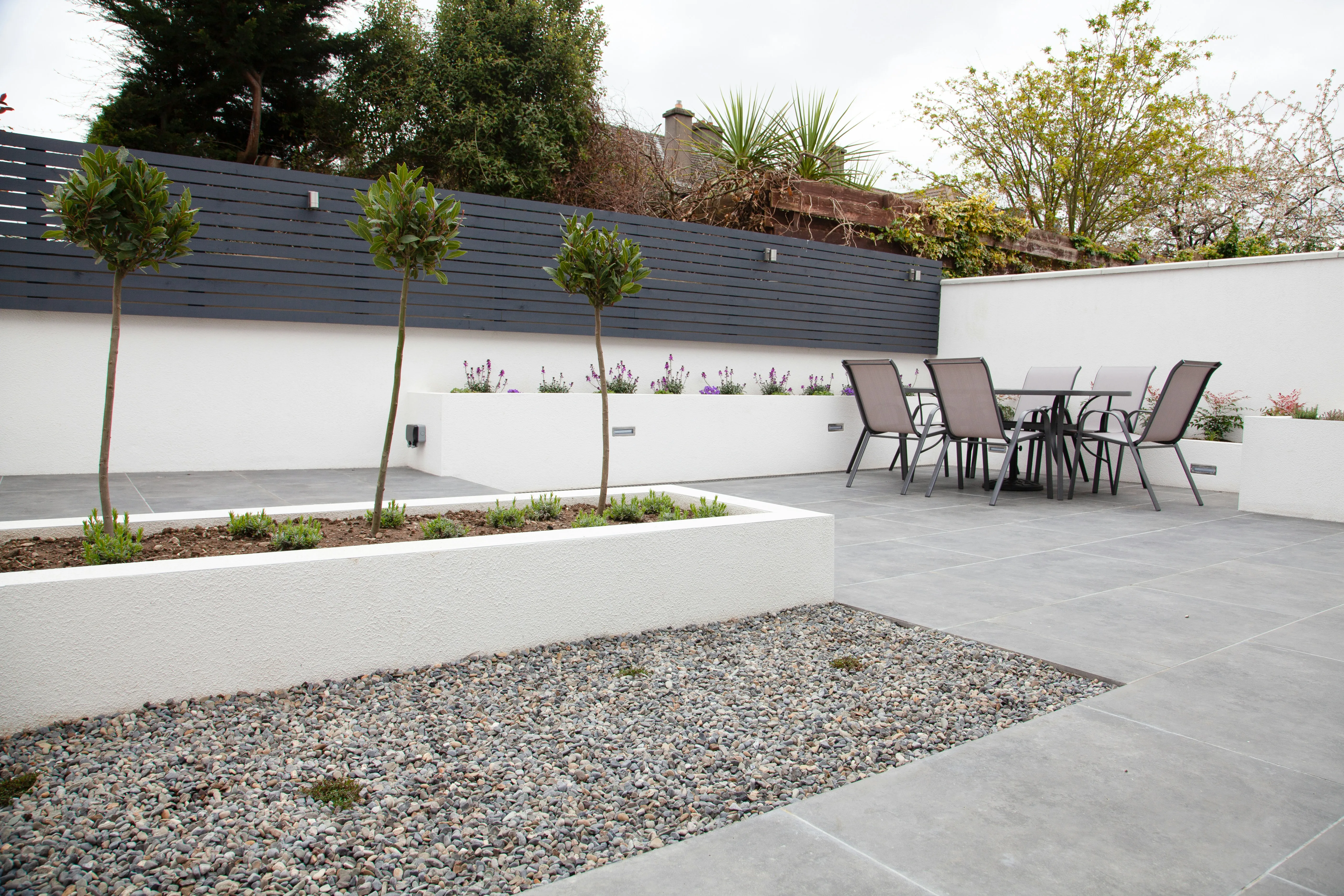 Modern grey paved patio with raised white planters and outdoor furniture