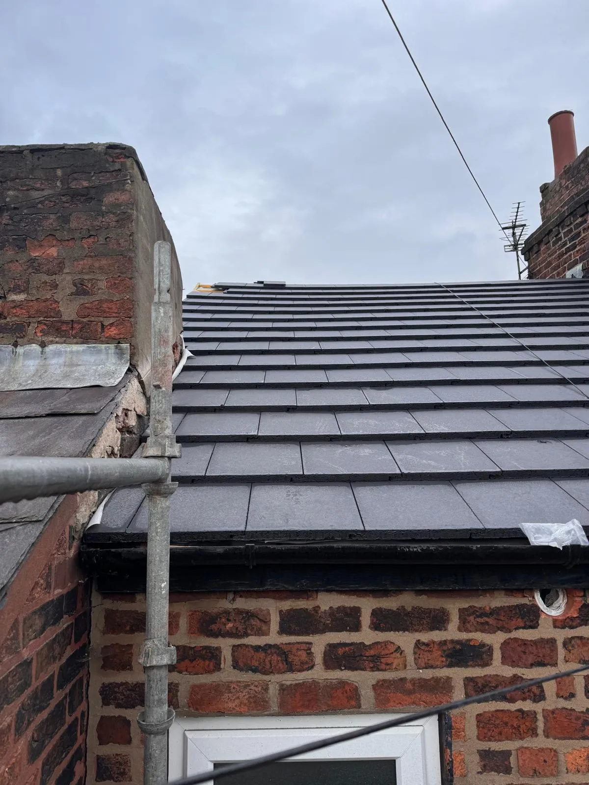 New dark grey tiled roof being installed or recently completed on a house, with scaffolding and brickwork visible.