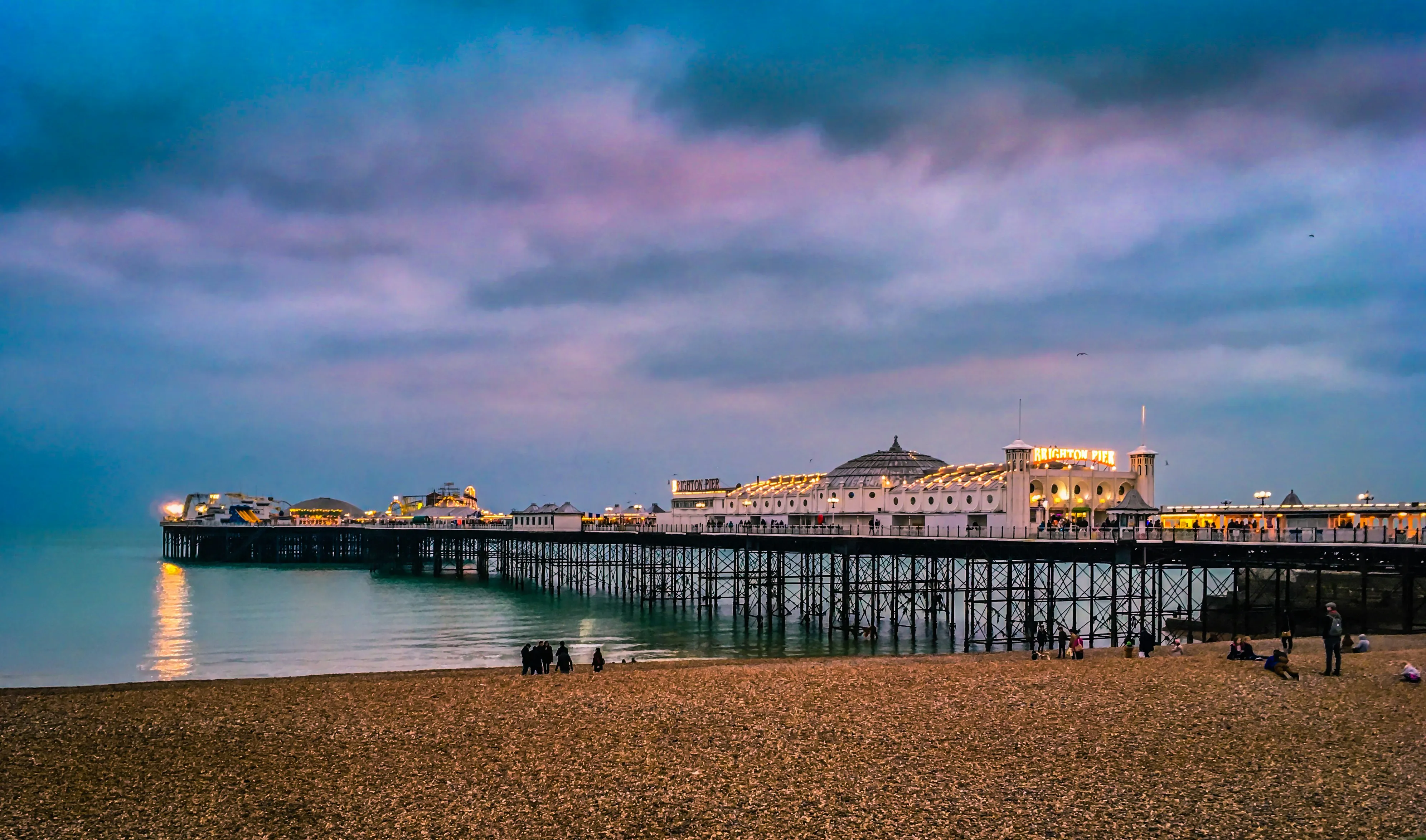 Brighton Pier lit up at night from the pebble beach, a landmark in our Brighton and Hove service area.