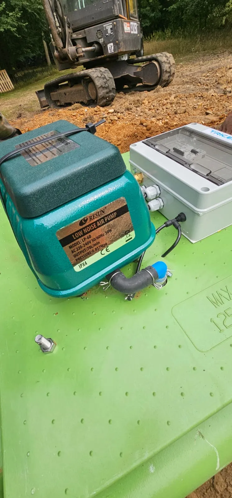 Components of a sewage treatment plant, including an air pump and control box, during installation on a construction site.