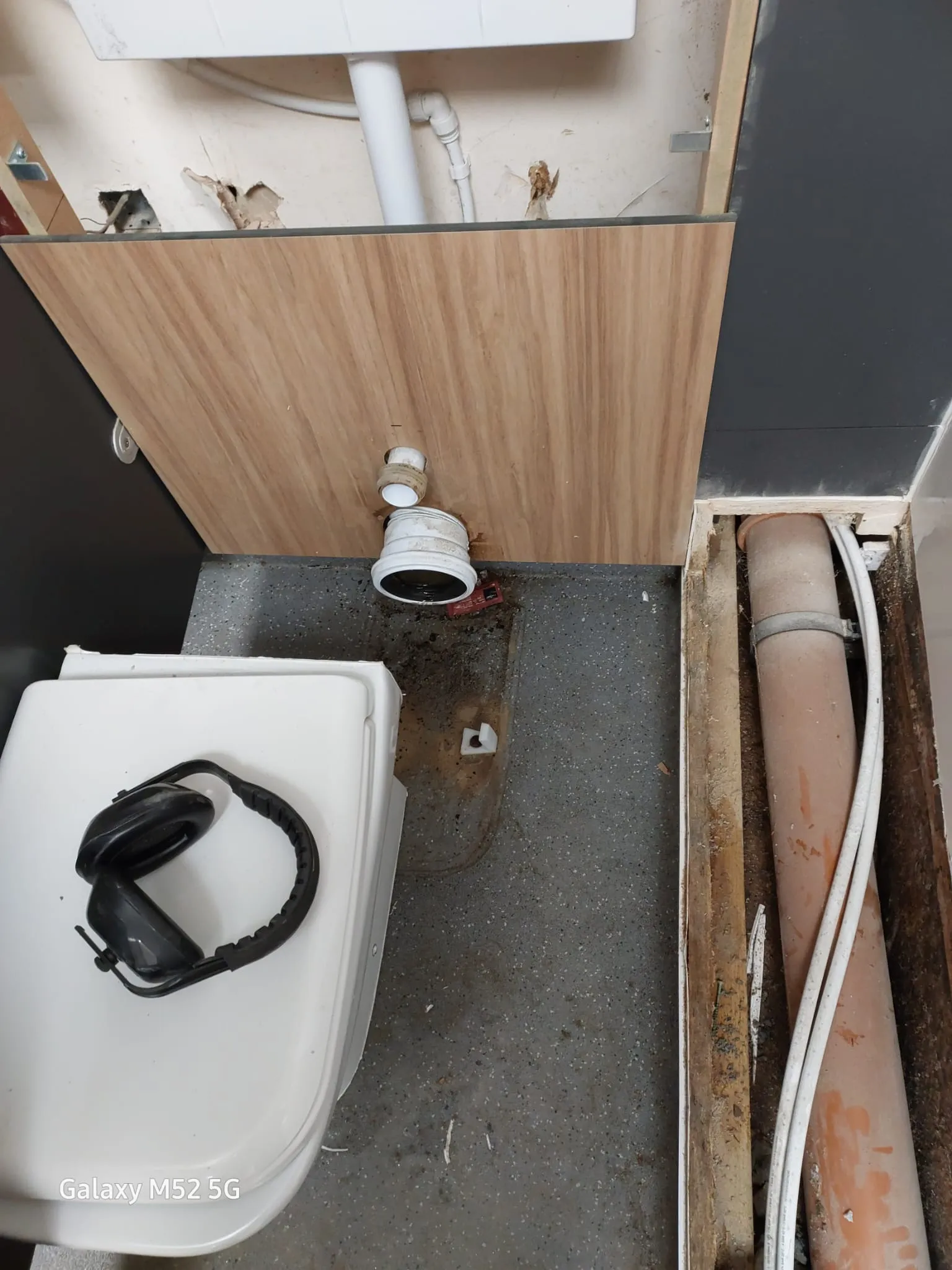 An overhead view of exposed drainage pipes, a toilet, and construction debris, indicating drain repair or new installation work.