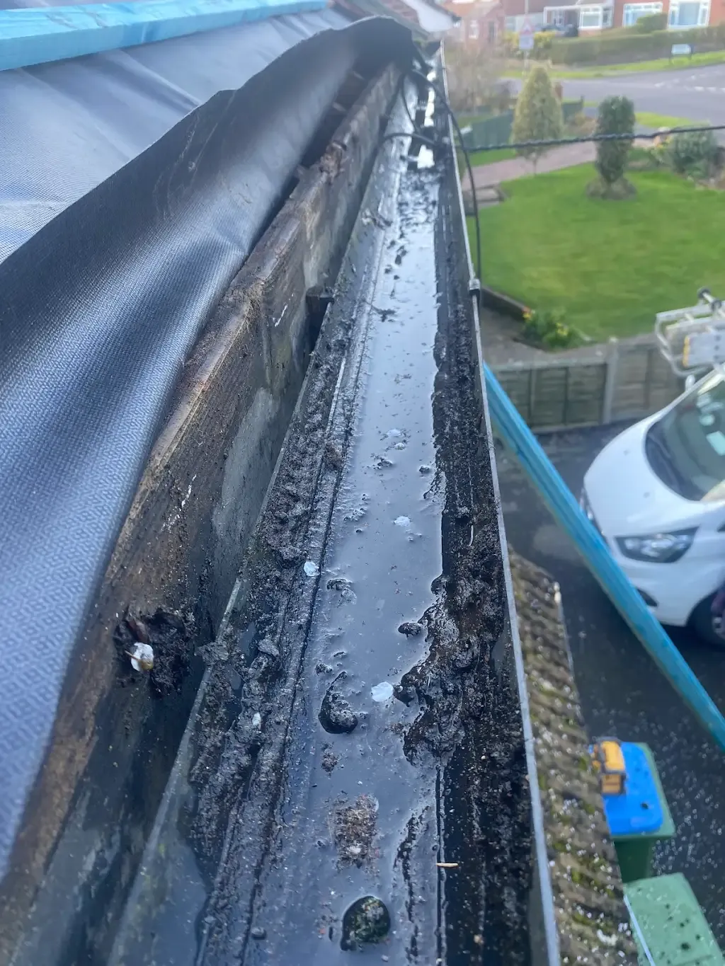 Blocked gutter overflowing with dirty water and debris.