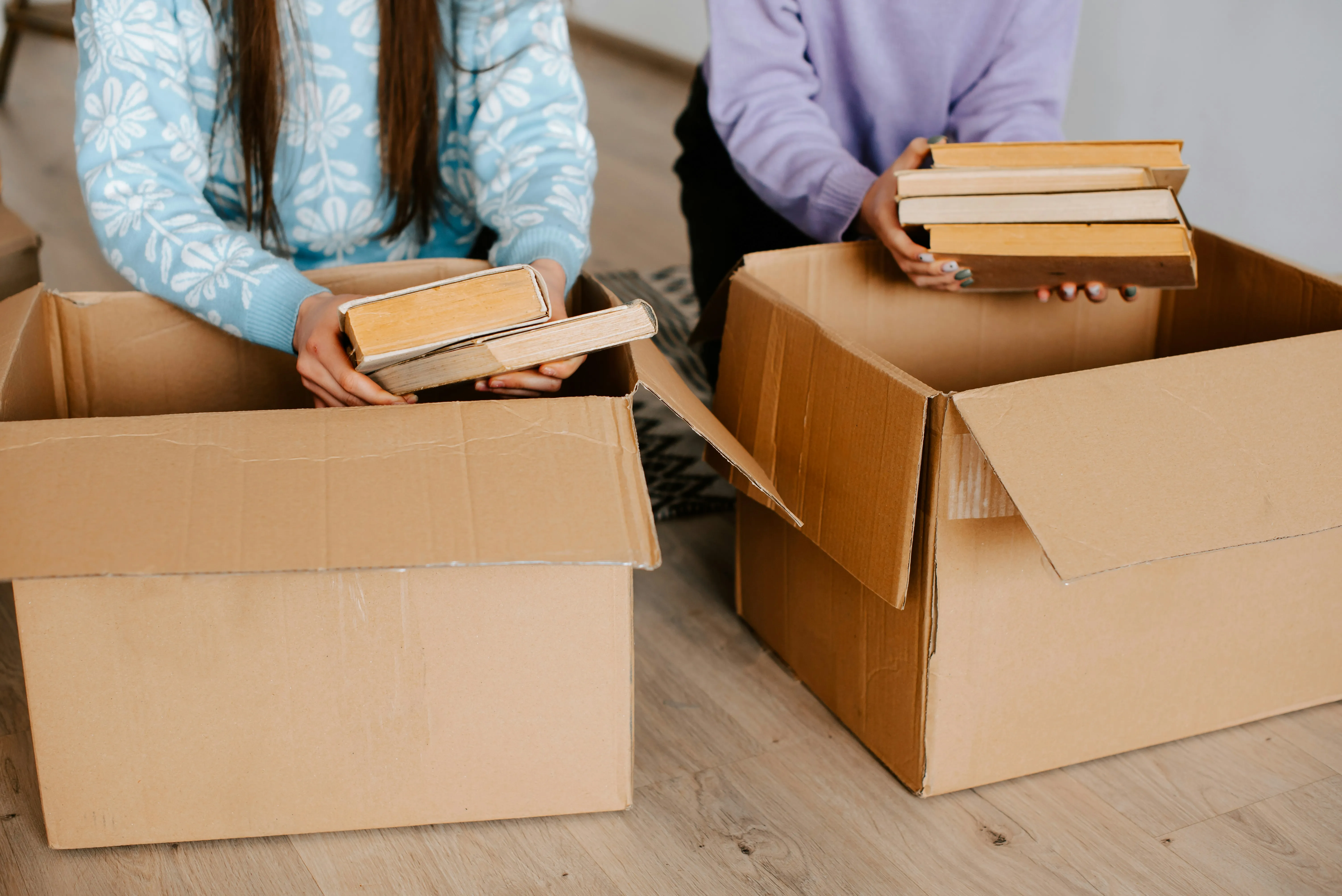 Hands placing books into cardboard boxes during packing for a house move.