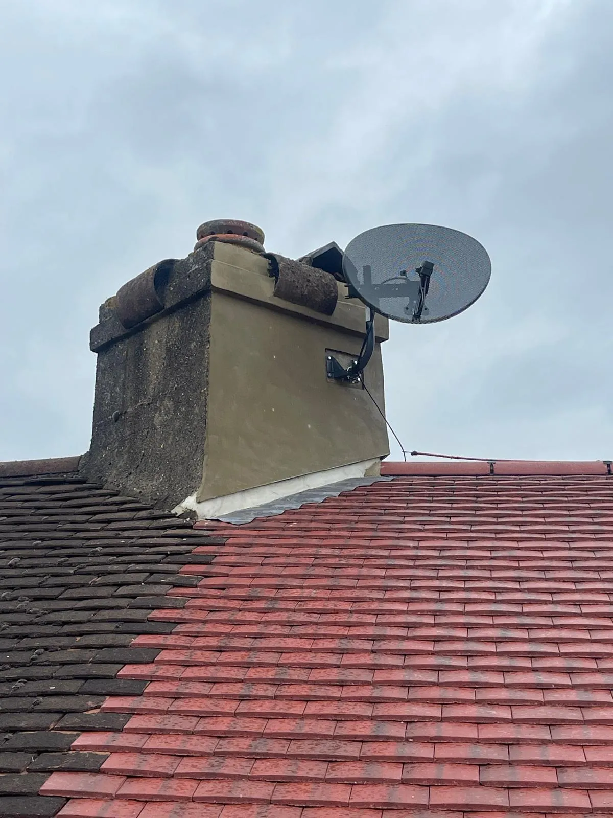 A chimney with a satellite dish on a residential tiled roof, showing new flashing and a mix of old and new red and dark roof tiles.