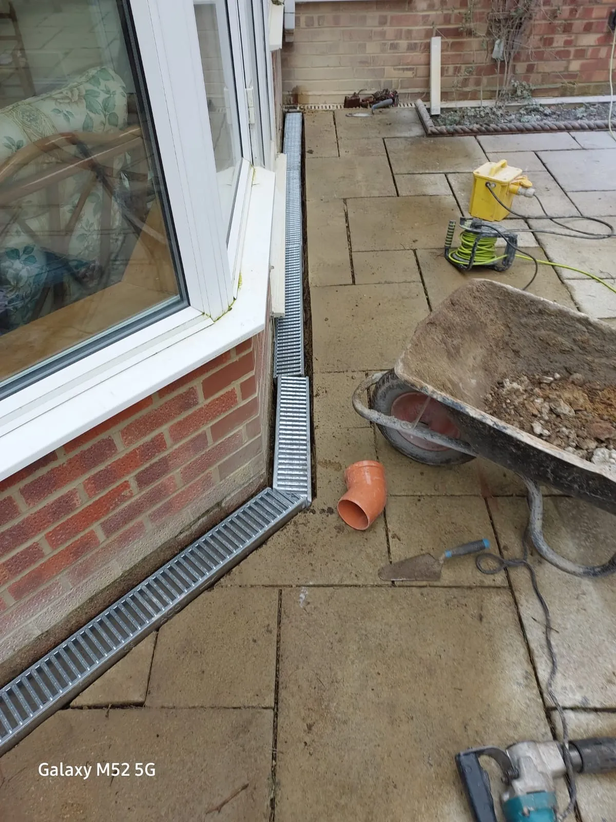 Installation of new ACO channel drainage on a residential patio next to a building wall.