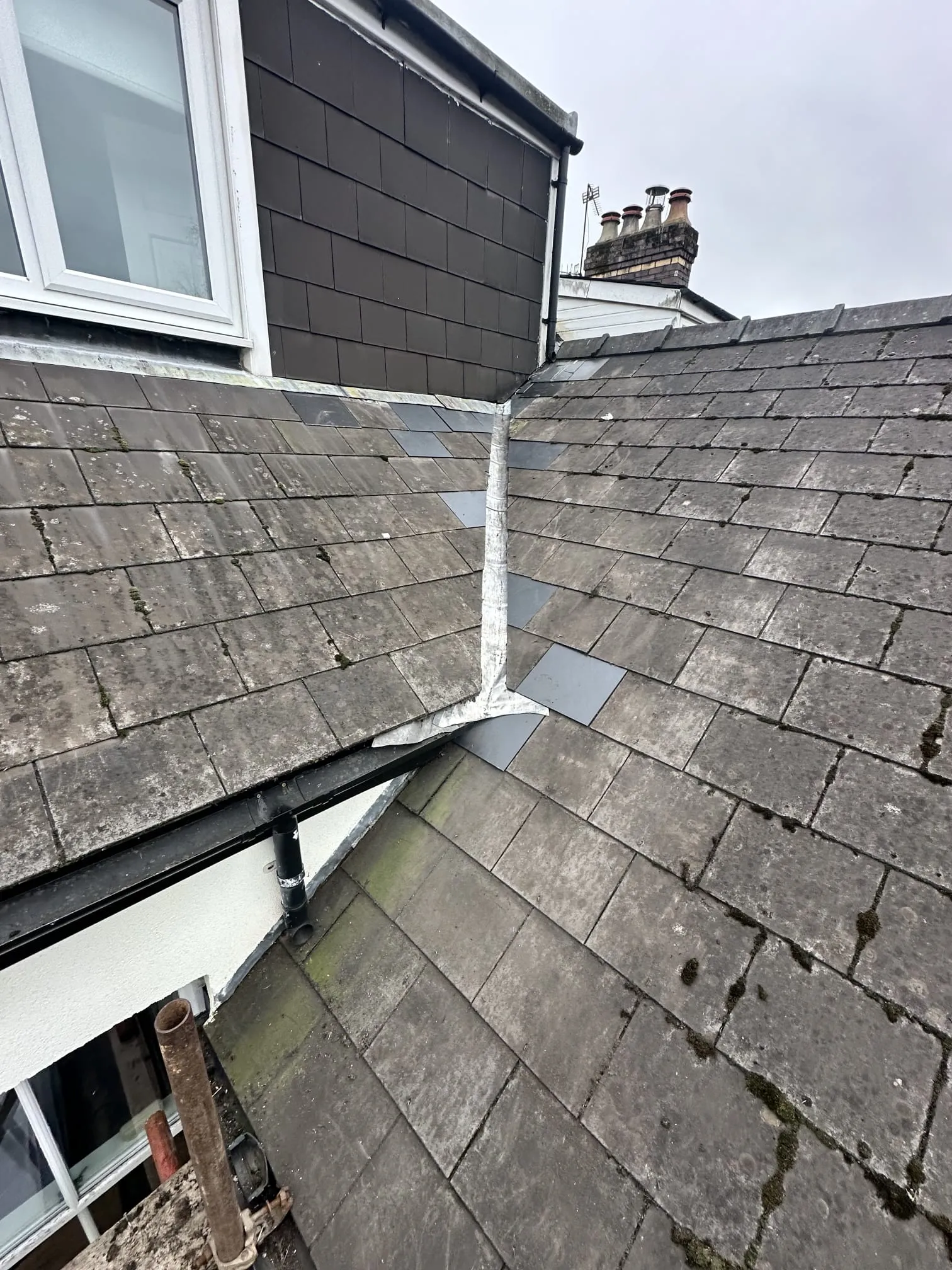 A residential pitched roof with old slate and tiles, moss, and a lead valley.