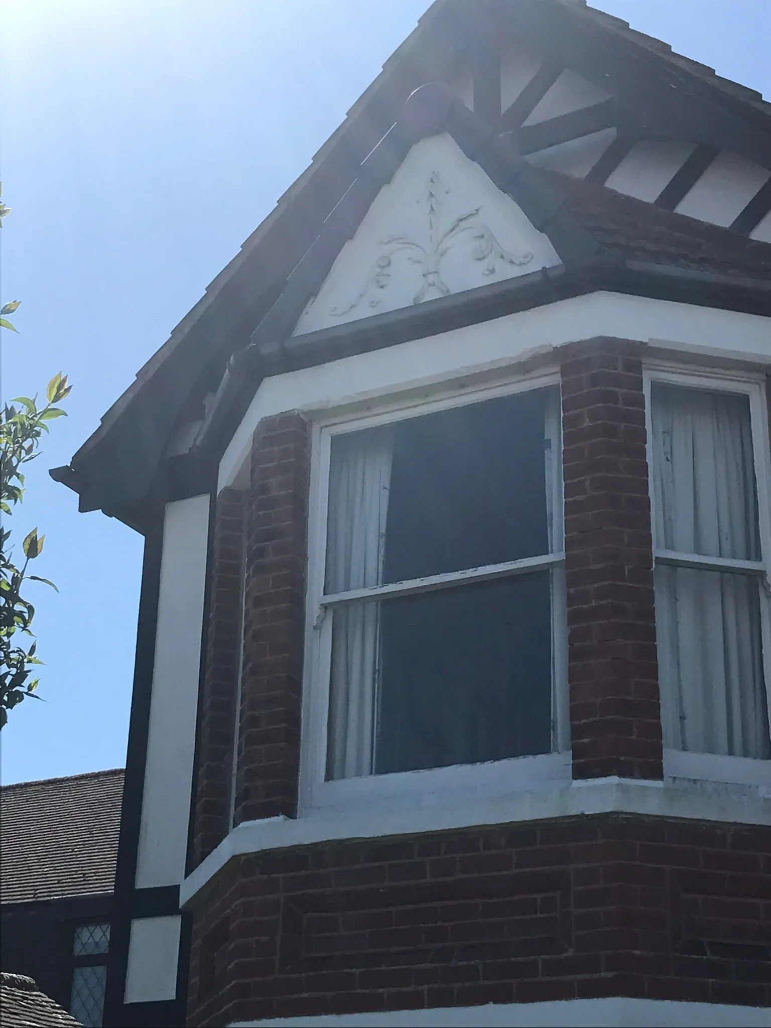 A picture of the upper exterior of a house, featuring a bay window, pitched roof, and decorative fascia work.