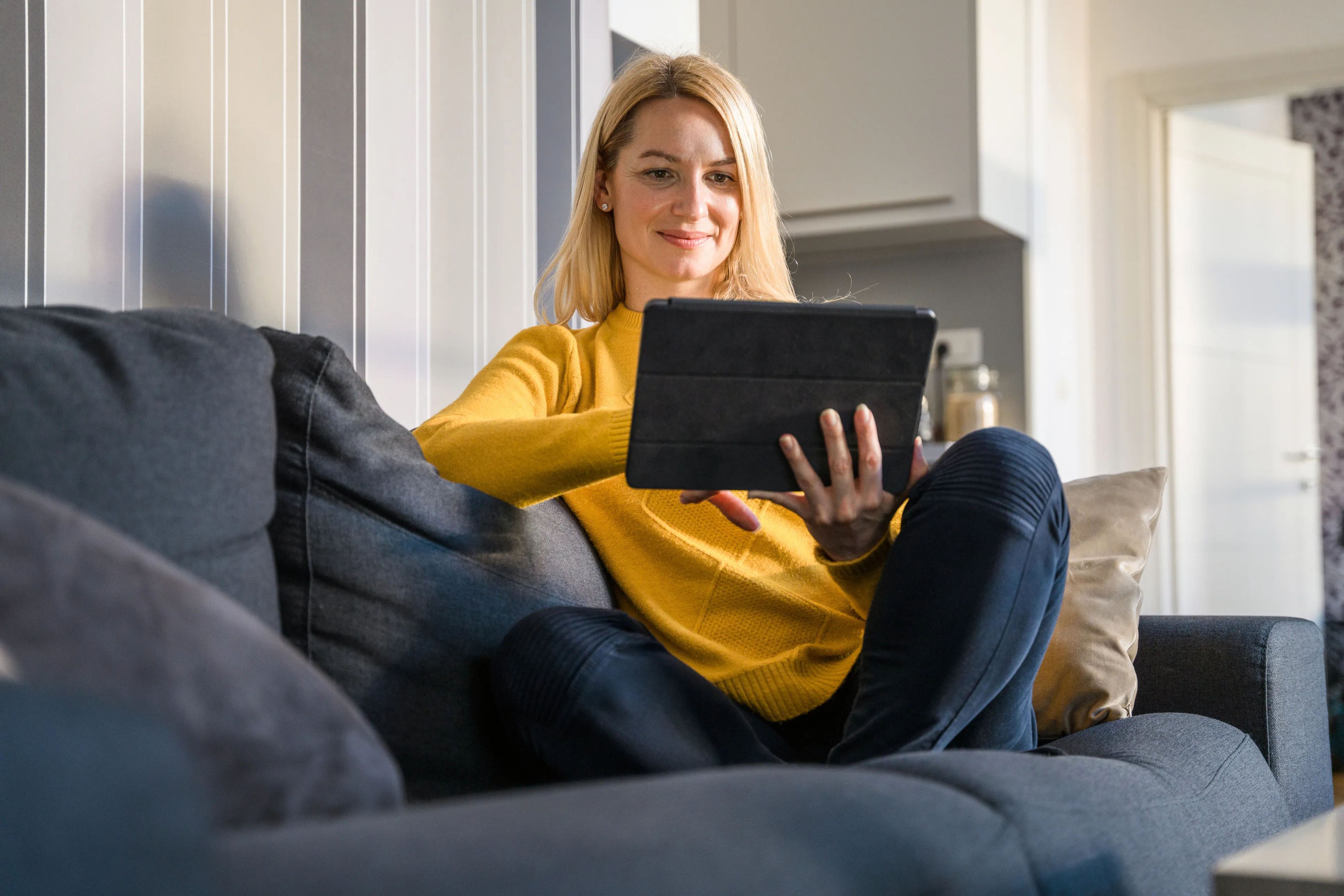 Woman using a tablet on a sofa, looking comfortable