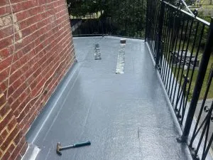 A newly completed grey flat roof installation on a residential balcony or terrace with a brick wall and metal railing.