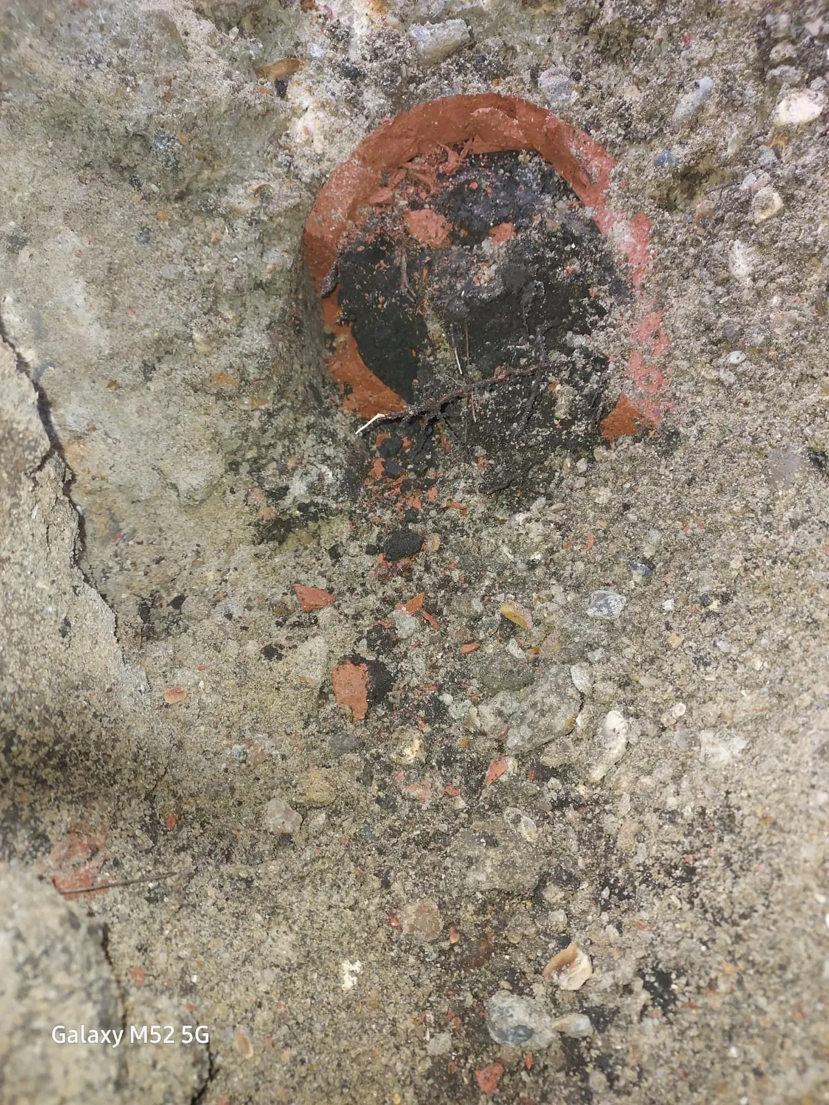 Close-up of a blocked drain pipe in excavated ground with dark sludge and debris.