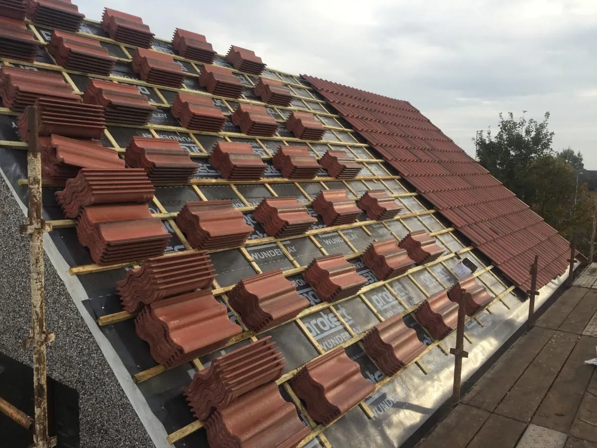 Roof retiling in progress with new red tiles on battens