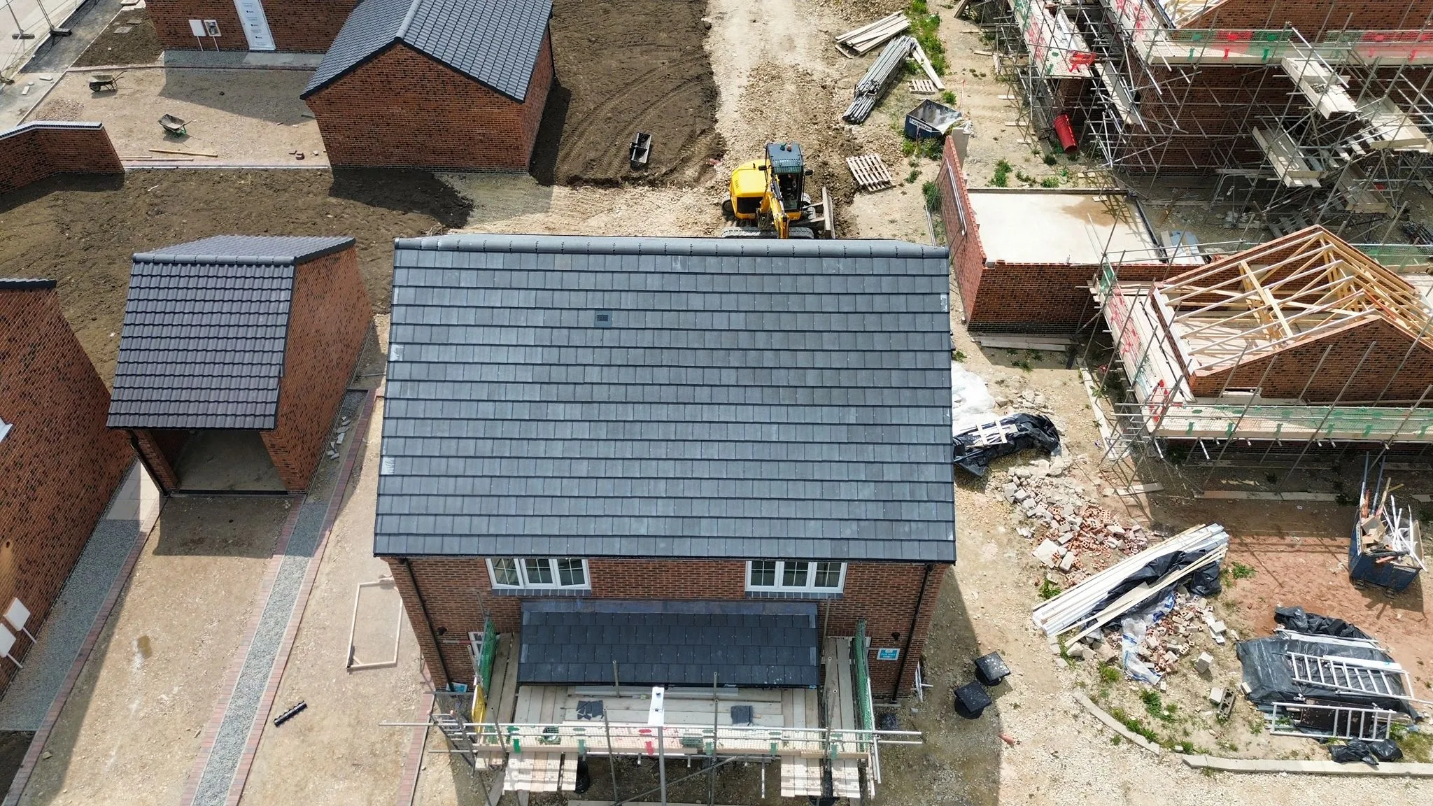 An aerial photo of new build houses in various stages of construction, featuring completed pitched roofs with dark grey tiles and exposed roof timbers on other properties, highlighting new roof installations.