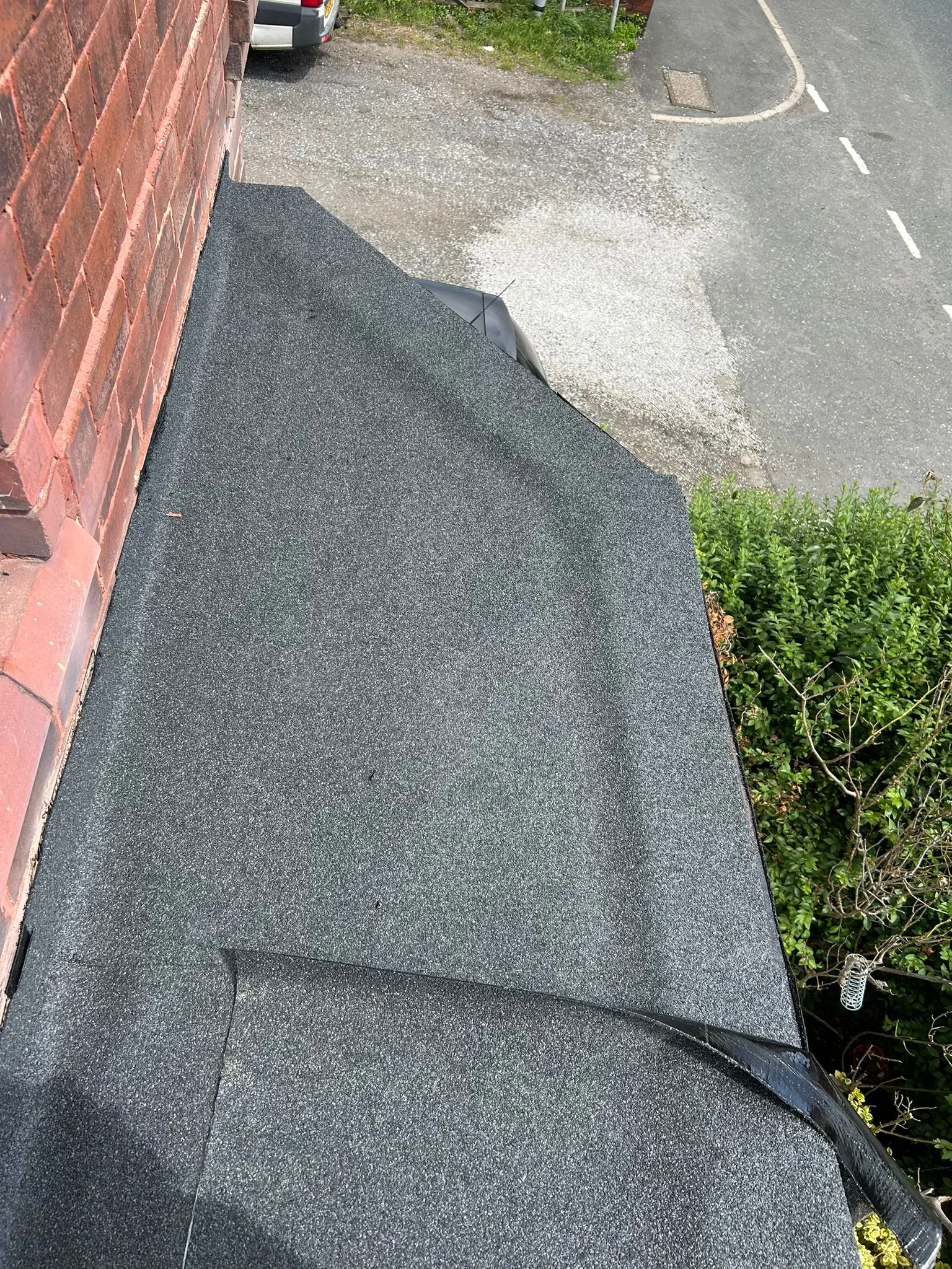 Close-up view of a new dark grey granular flat roof installed alongside a red brick residential wall.