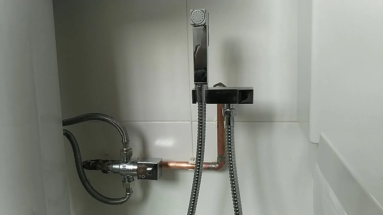 Newly installed chrome thermostatic mixing valve and handheld shower sprayer on a white tiled wall