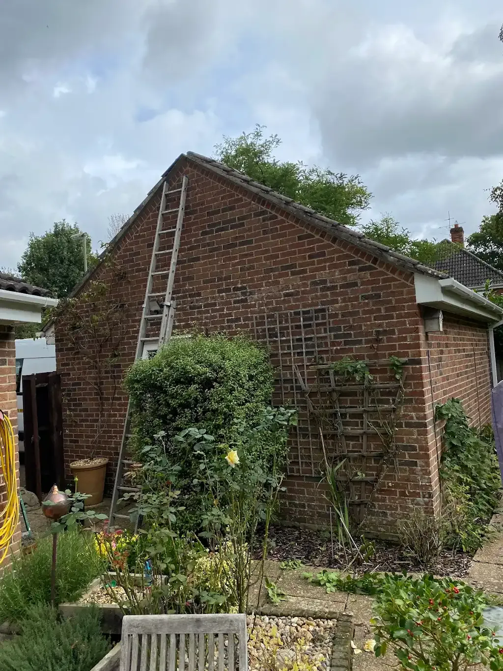 Side of a residential building with a tiled roof and a ladder leaning against the wall.
