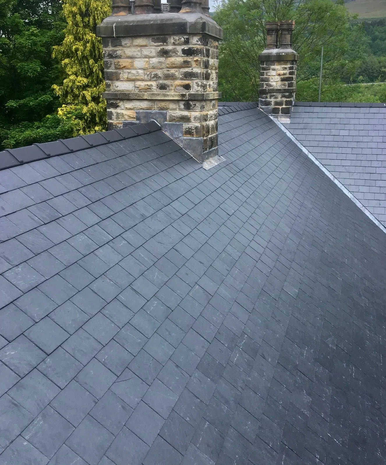 Dark grey tiled roof with brick chimneys and lead flashing