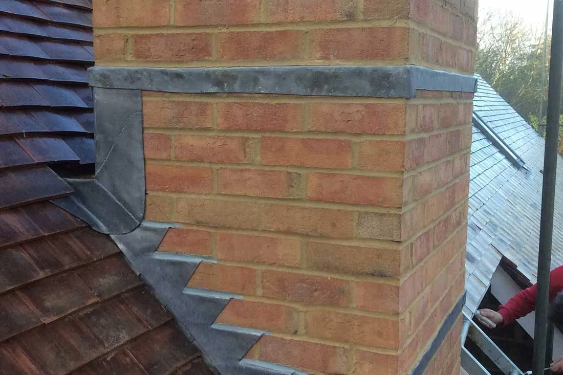 Expertly installed lead flashing around a brick chimney on a tiled roof.