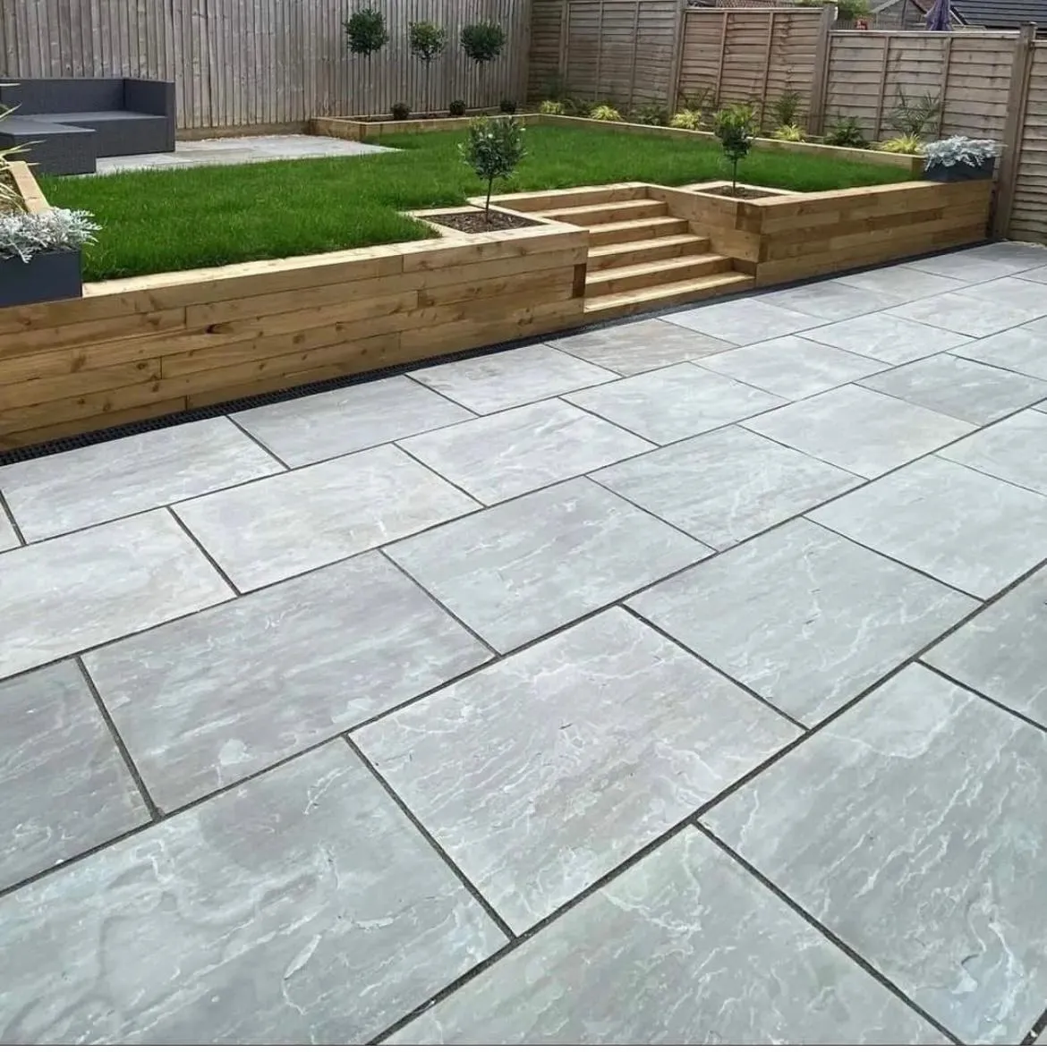 Modern grey slab patio with raised sleeper garden beds and artificial grass