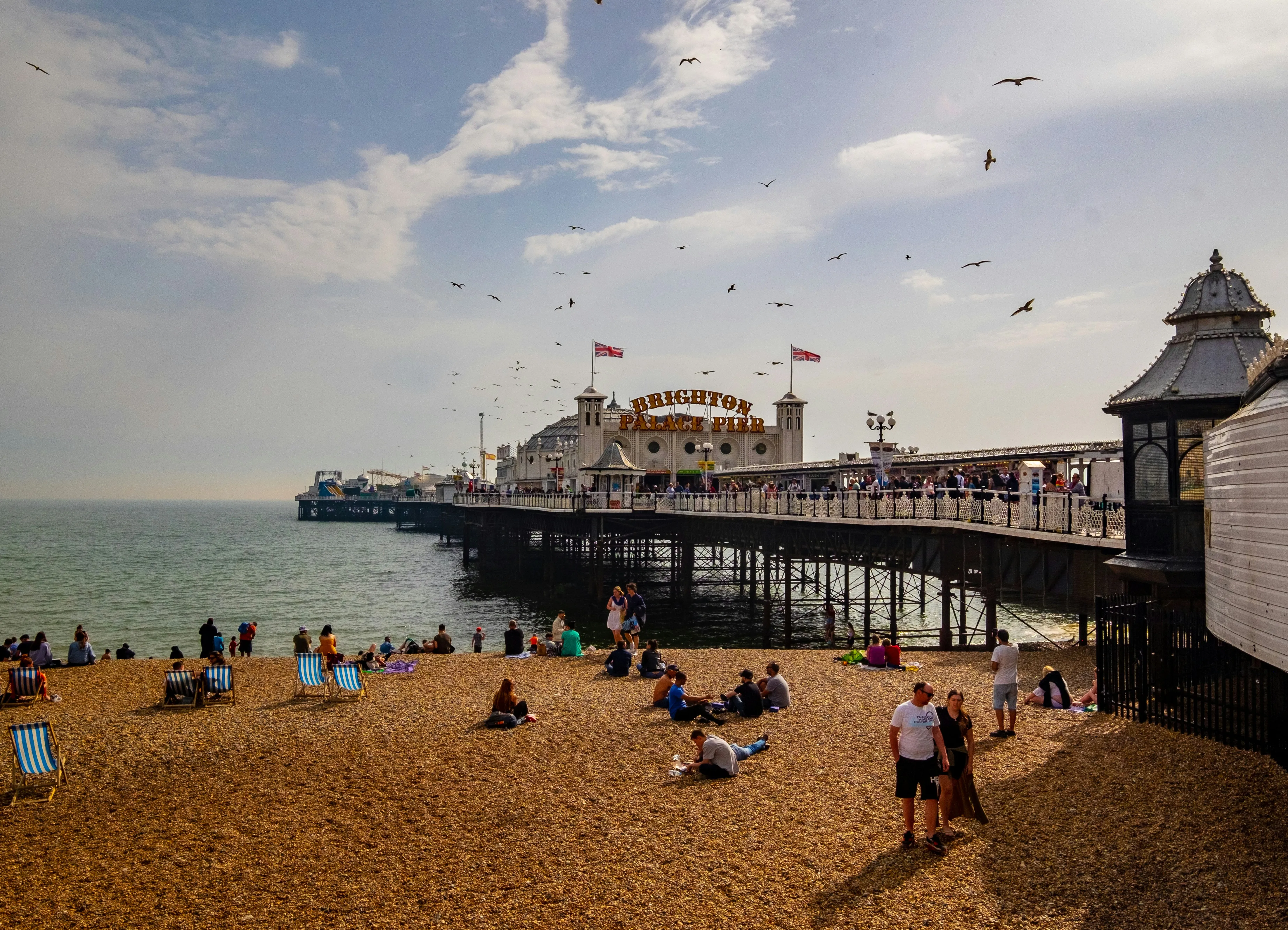 Brighton Palace Pier on a sunny day with people on the pebble beach and seagulls in the sky.