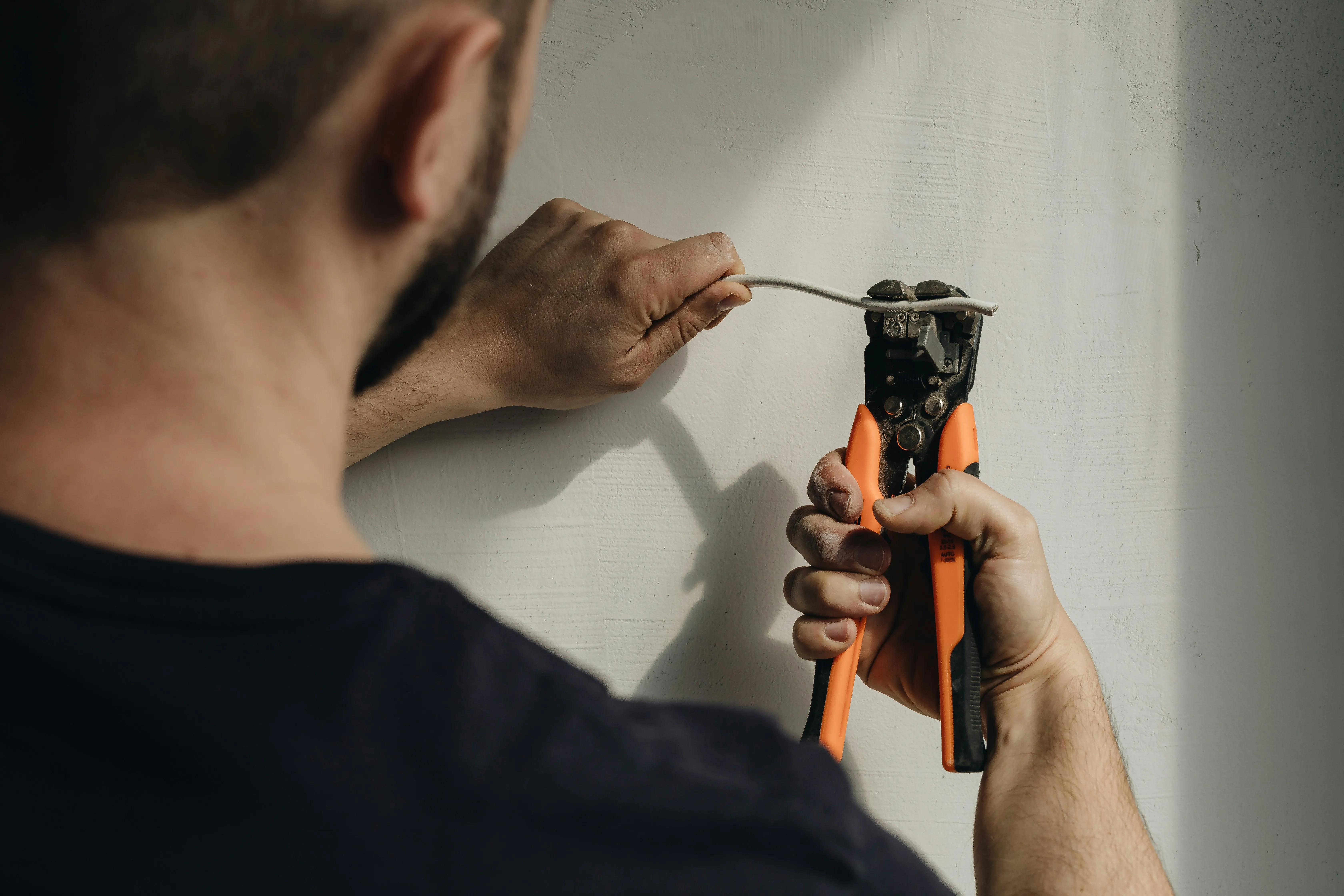 Electrician stripping a white electrical wire with orange wire strippers.