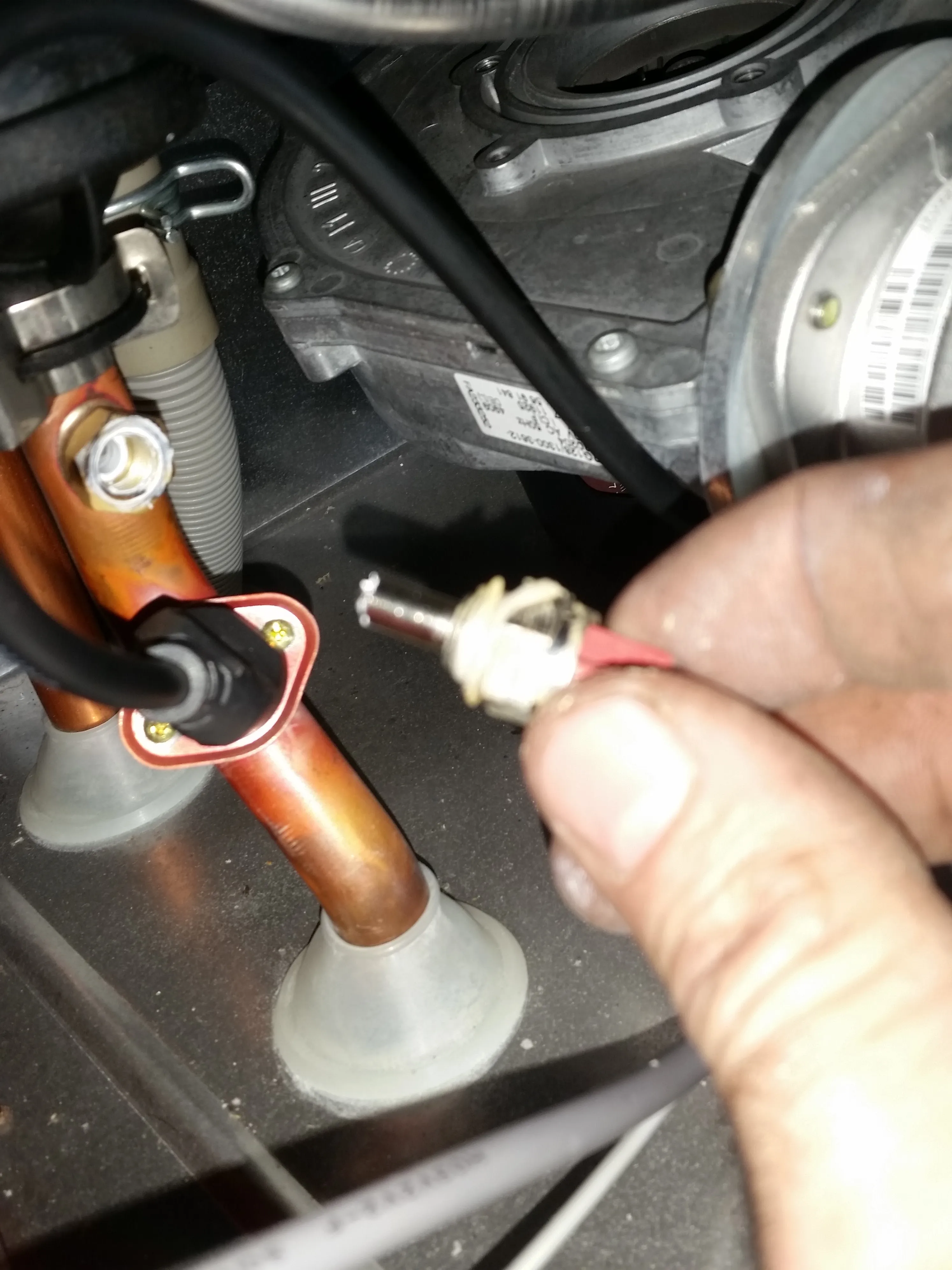 Plumber's hand working on boiler pipes and wires during a repair or service.