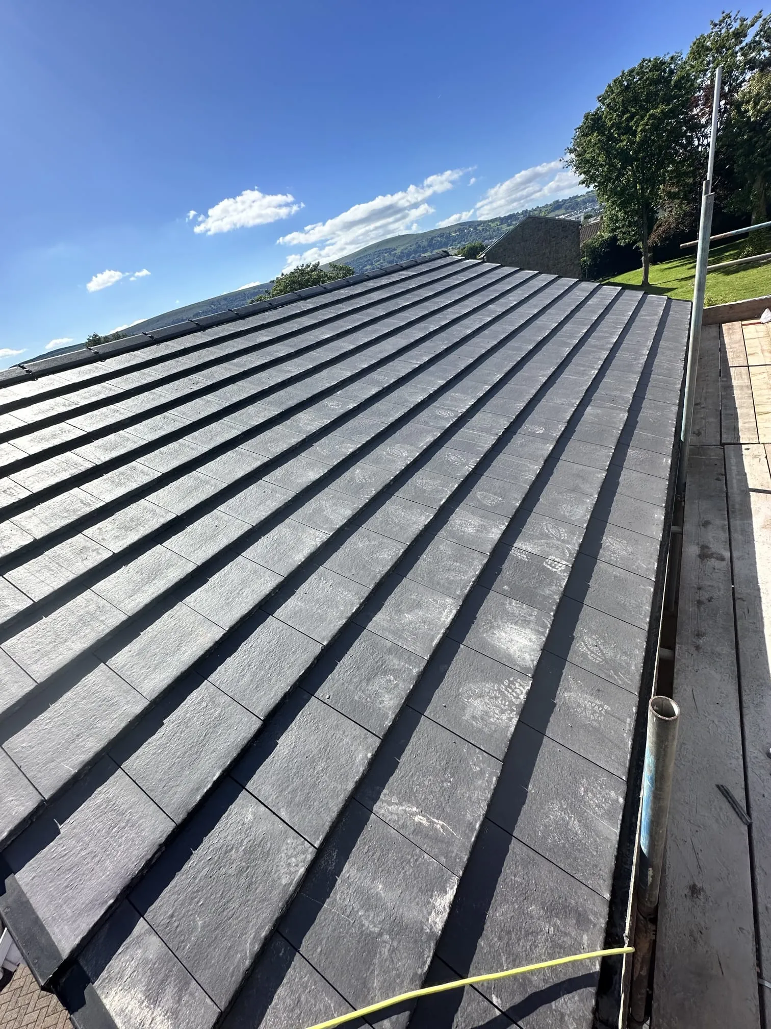 Newly installed dark grey tiled or slate roof under a bright blue sky.