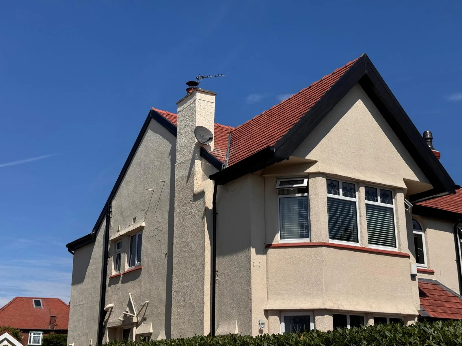 A residential property featuring a newly installed or well-maintained red tiled roof, black roofline elements, and a chimney.