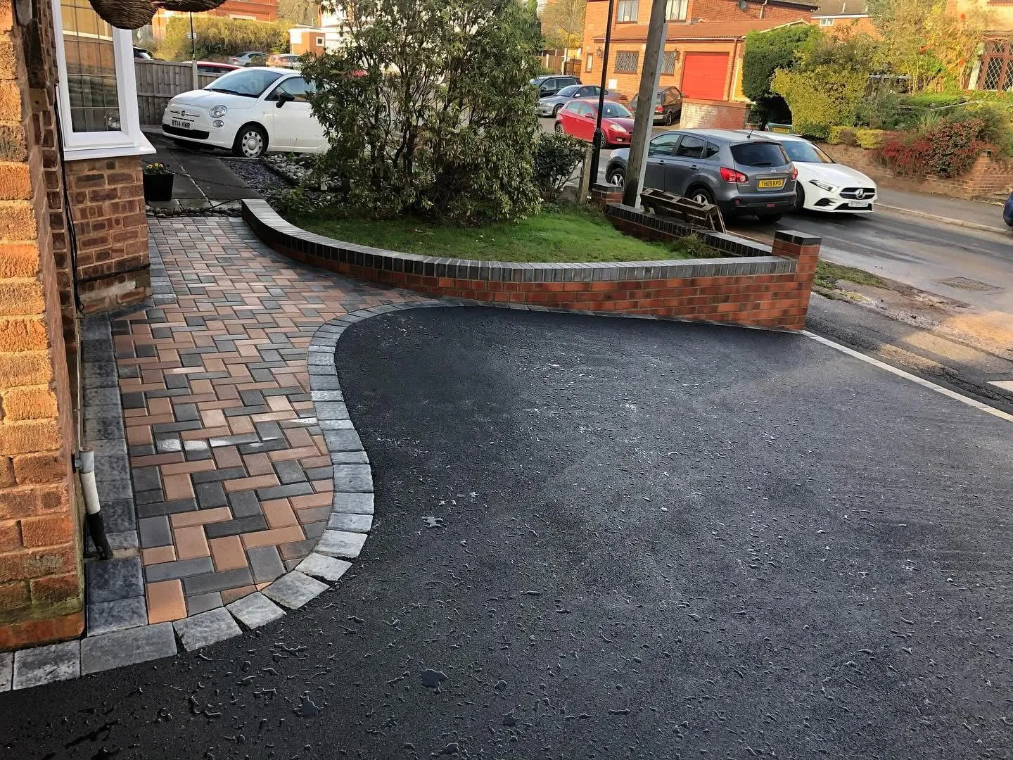 Newly installed tarmac and block paving driveway with a curved design, adjacent to a brick house and a low garden wall.