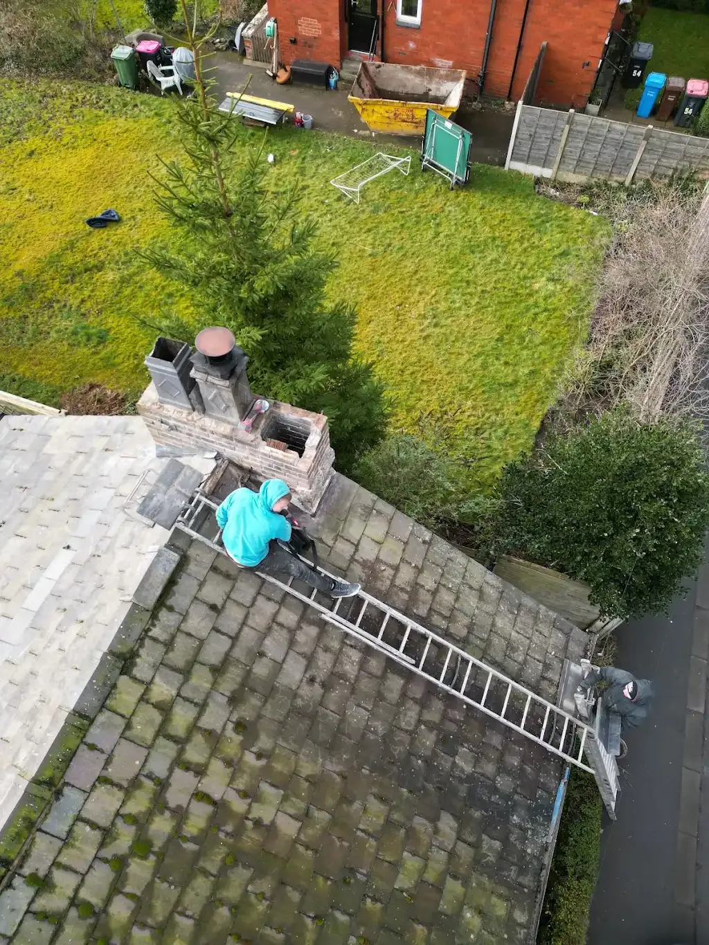 Two roofers on a tiled roof, one working near a chimney stack