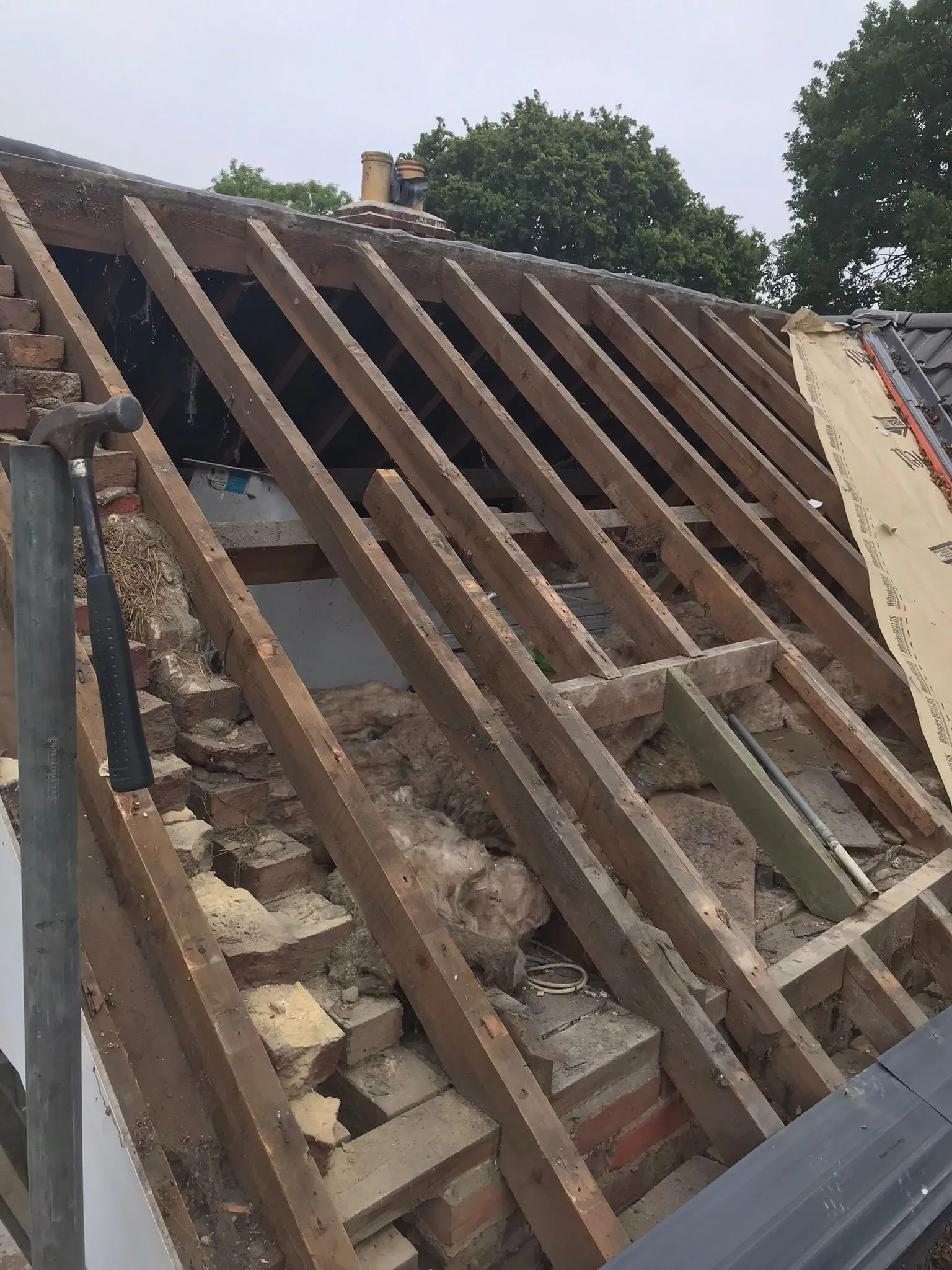 Roof renovation in progress showing exposed wooden rafters, insulation, and a hammer.
