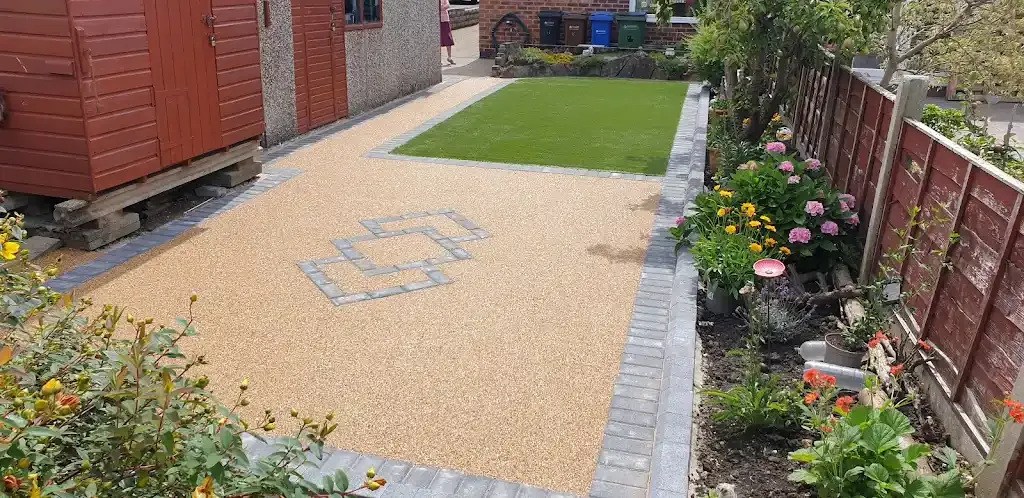 Newly installed resin bound driveway or patio with block paving border and artificial grass.